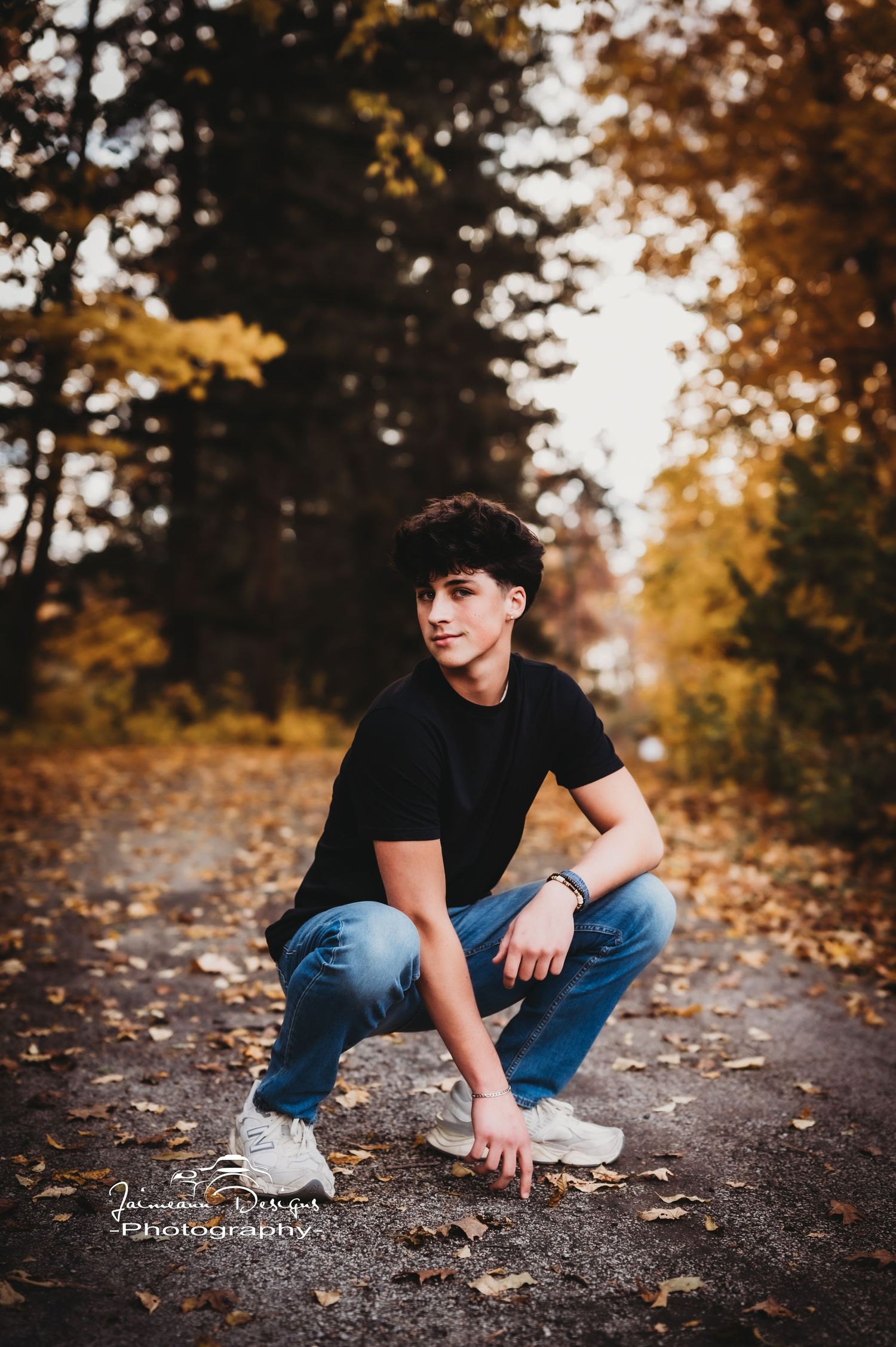 Crouching pose on autumn path with fallen leaves and golden trees in background.