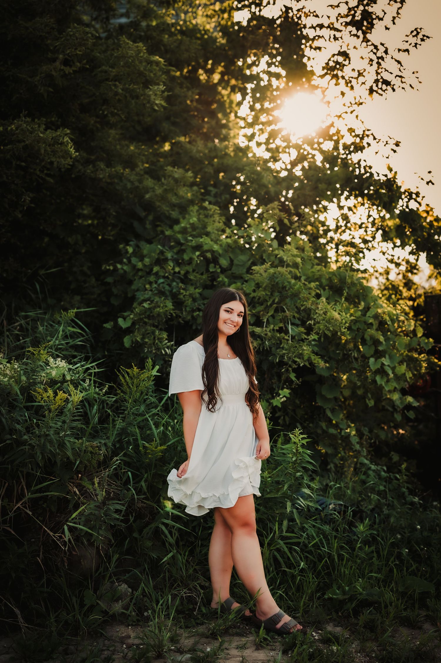 A white dress captures golden hour light against lush greenery in a romantic outdoor portrait session.