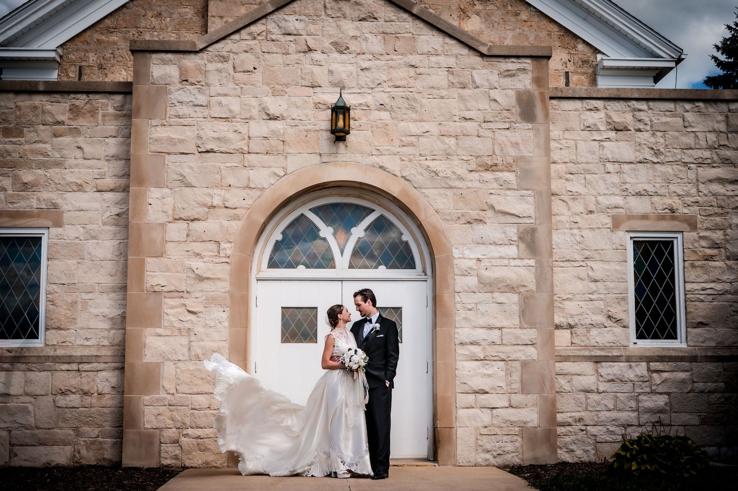 Wedding couple portraits outside a beautiful stone church with arched windows and classic architecture.