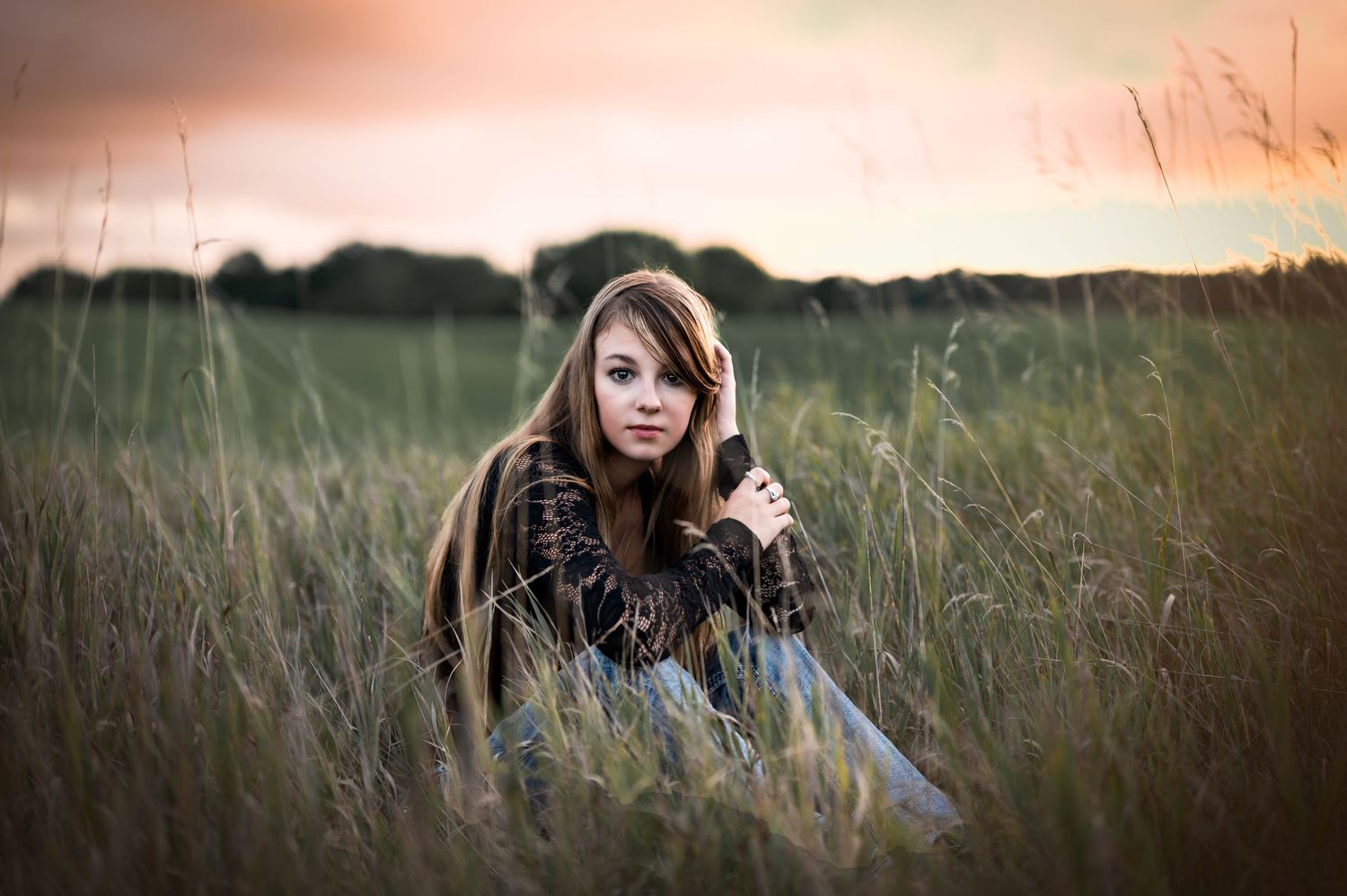 A person with long brown hair sits in a field of tall grass during golden hour sunset in Slinger, WI