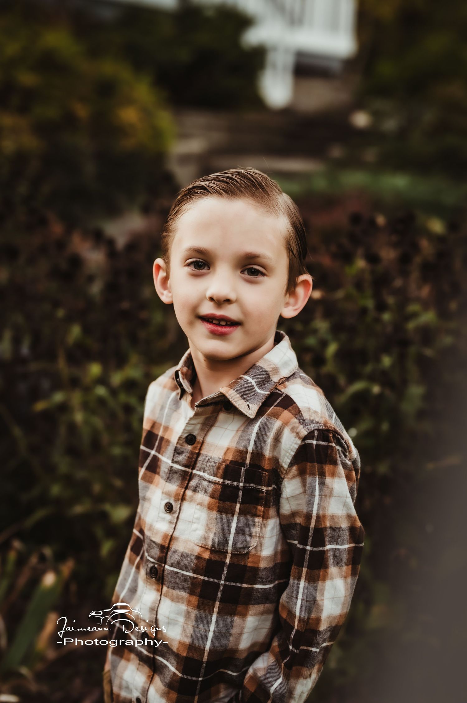A child in plaid flannel shirt smiles at camera in outdoor autumn setting.