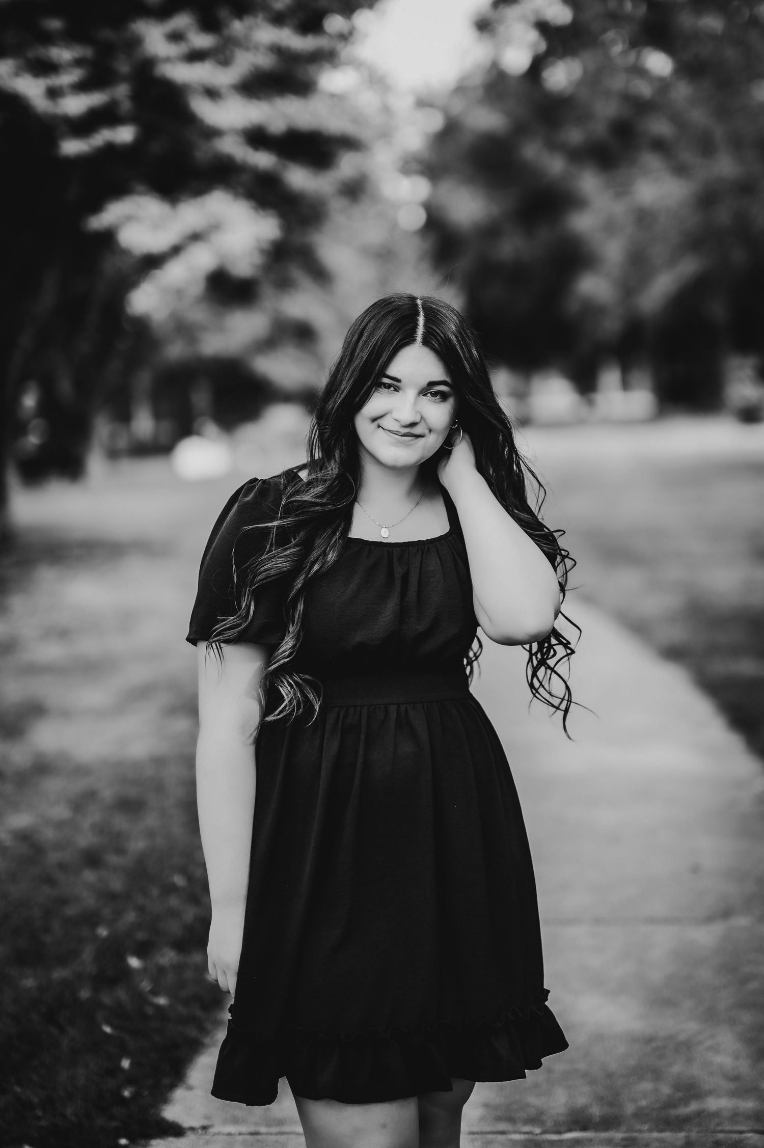 Black and white portrait on a tree-lined path showing elegant black dress.