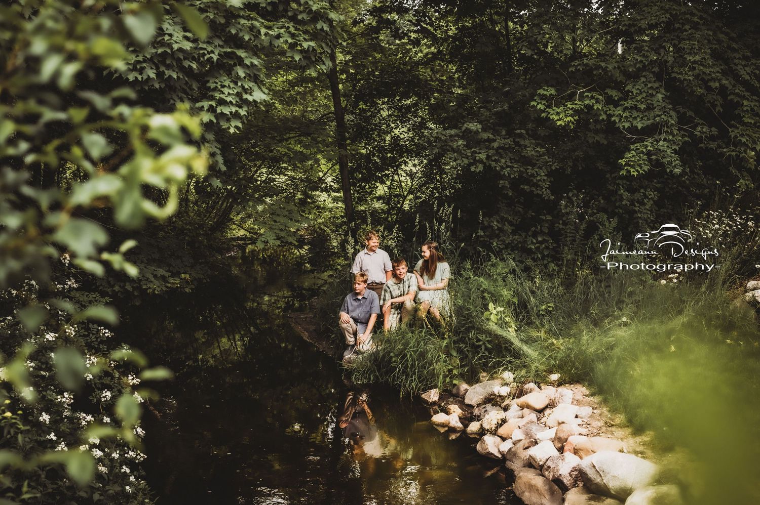 A candid family photo taken from above as they gather near a rocky stream in the woods.