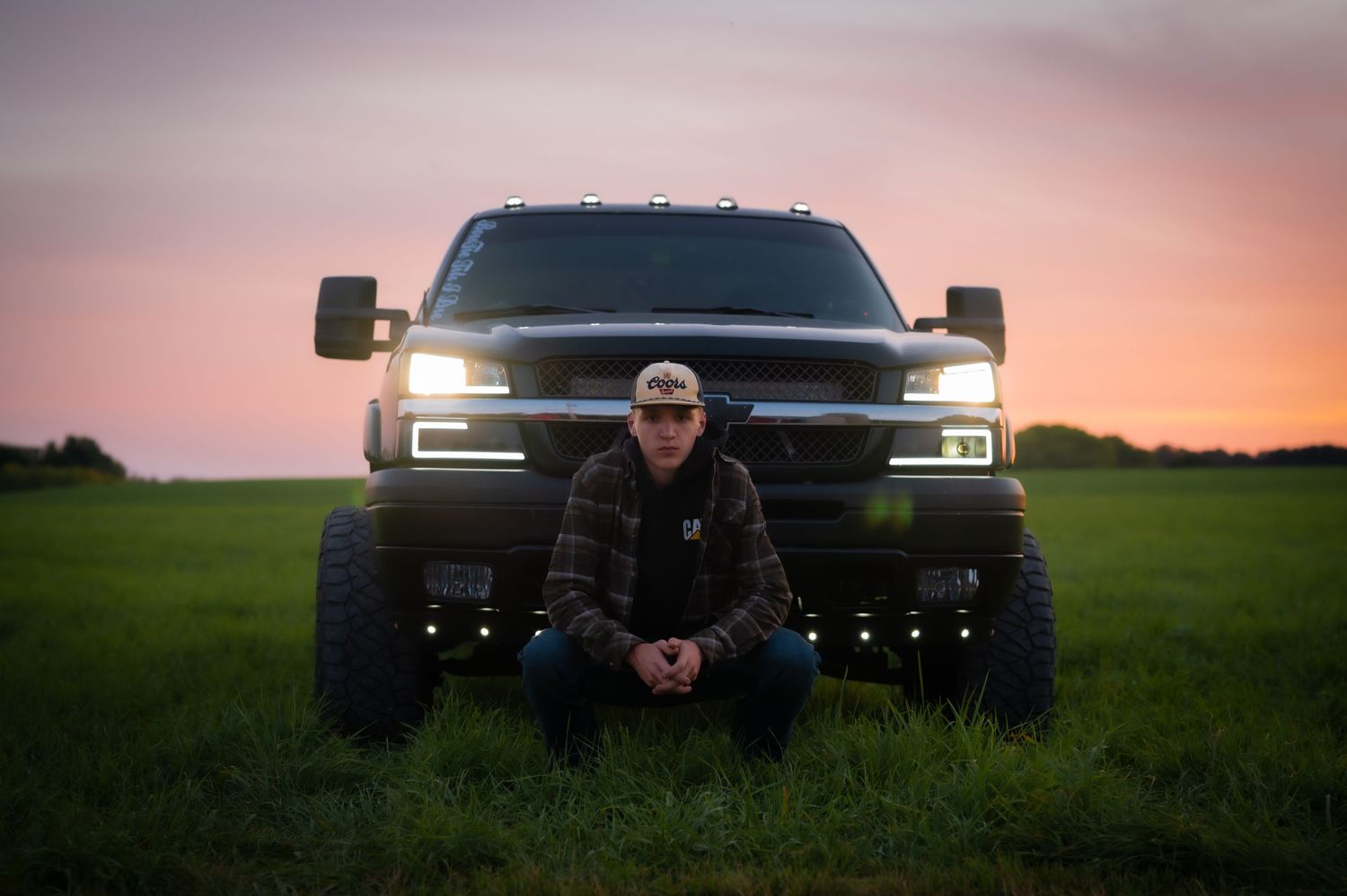 Modified black pickup truck with LED lights in green field at dusk.