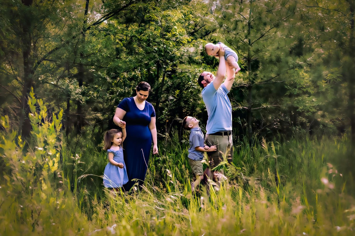 A family enjoys a playful moment together in a sunlit meadow surrounded by lush green vegetation near Fond du lac, WI