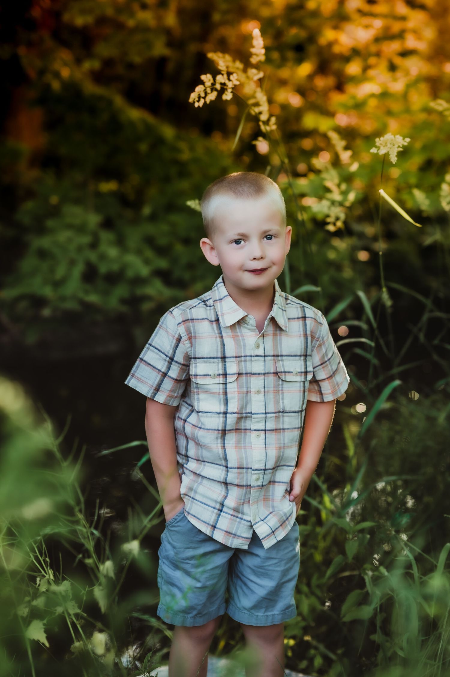 Child in plaid shirt poses for portrait among wildflowers and greenery.