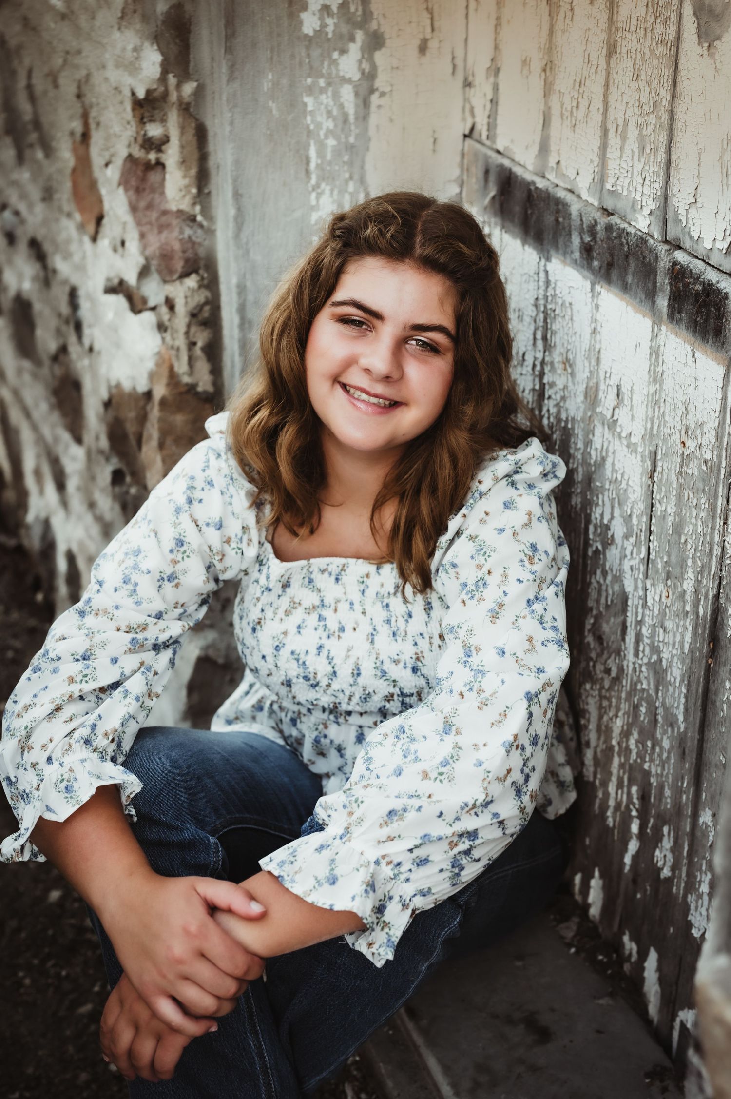 Portrait against weathered white wall wearing floral print top and jeans.