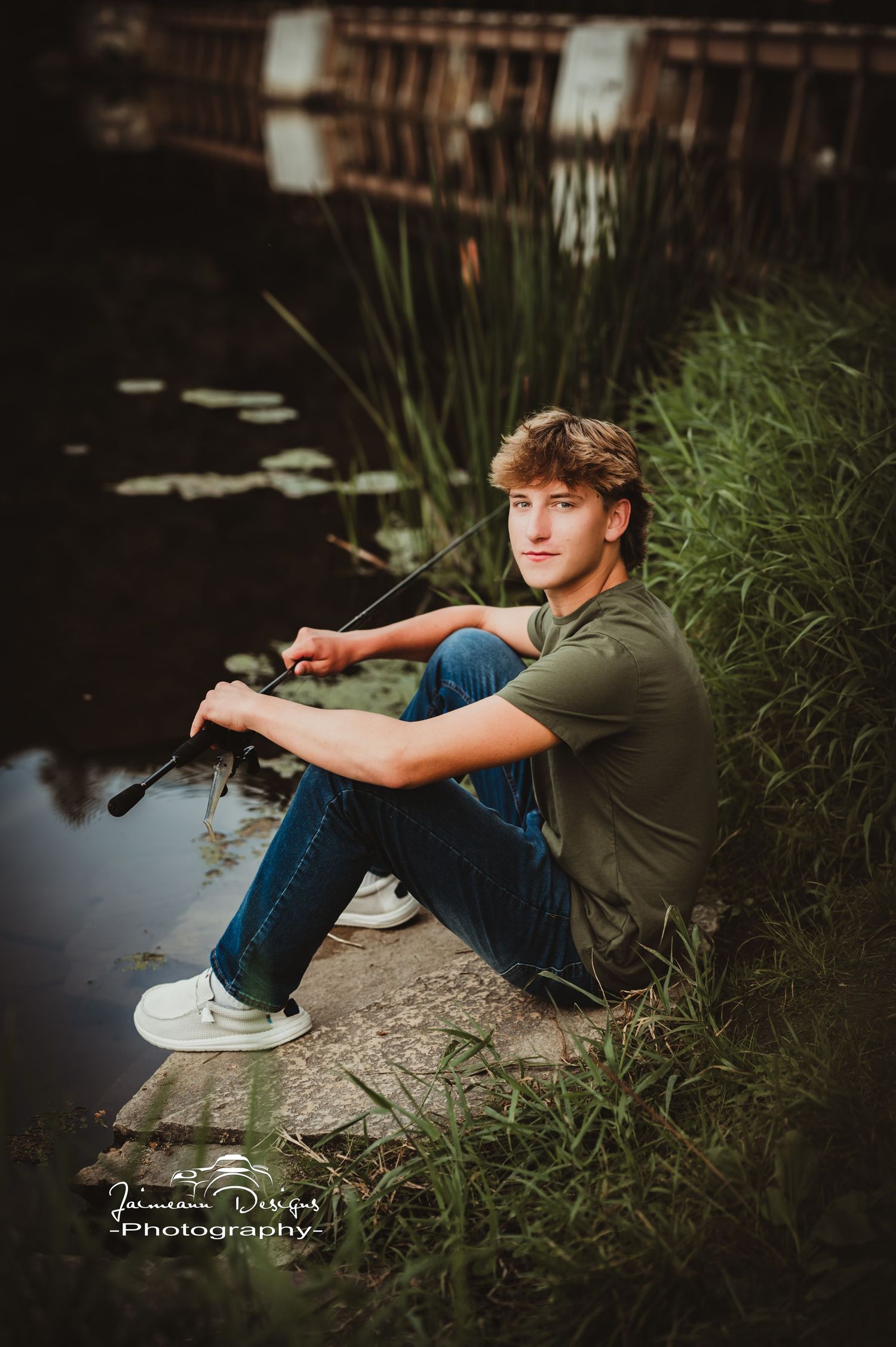 Person relaxing by water's edge surrounded by reeds and cattails.