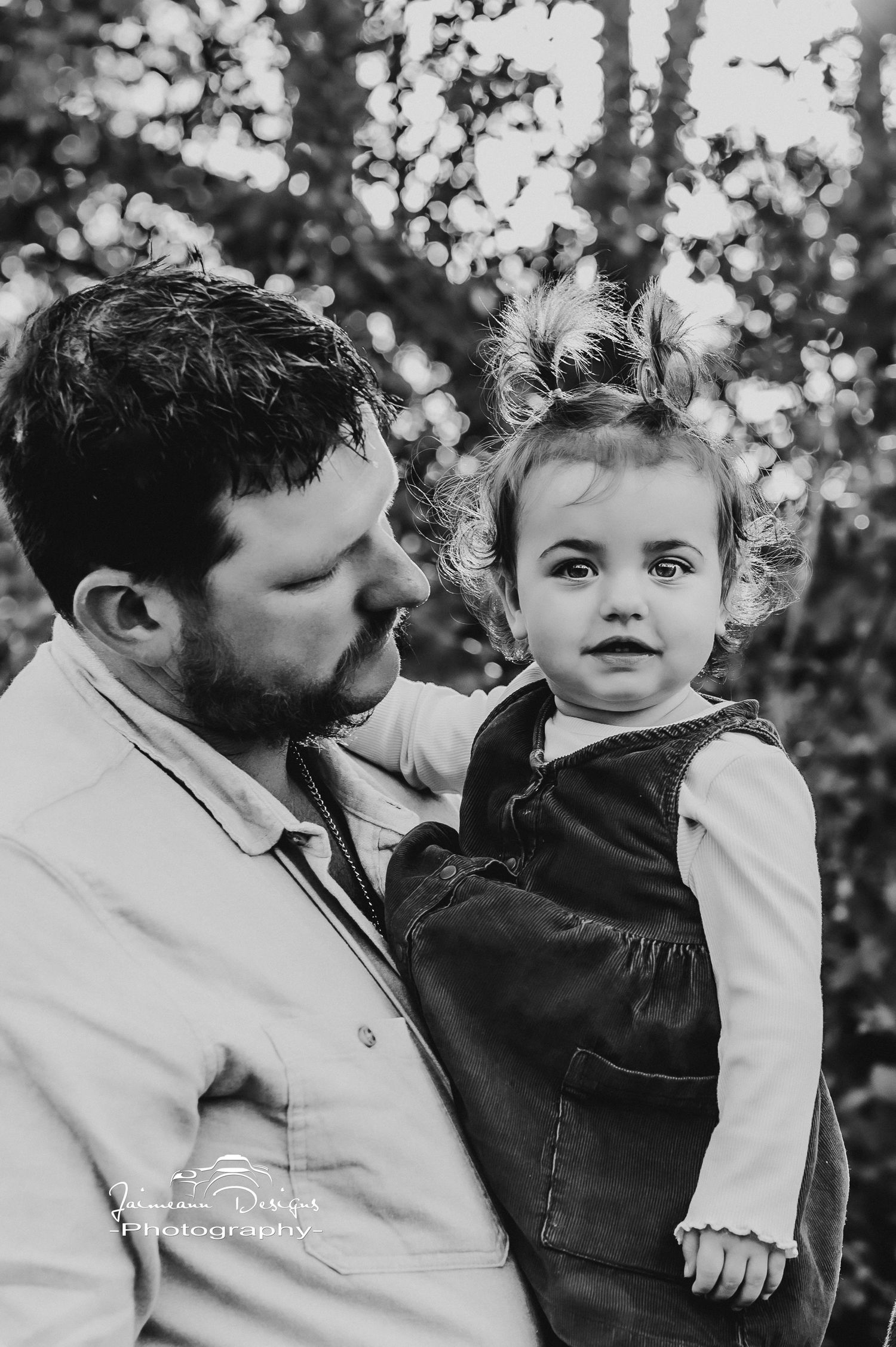 A tender black and white portrait taken in a forest with soft bokeh lighting in the background.