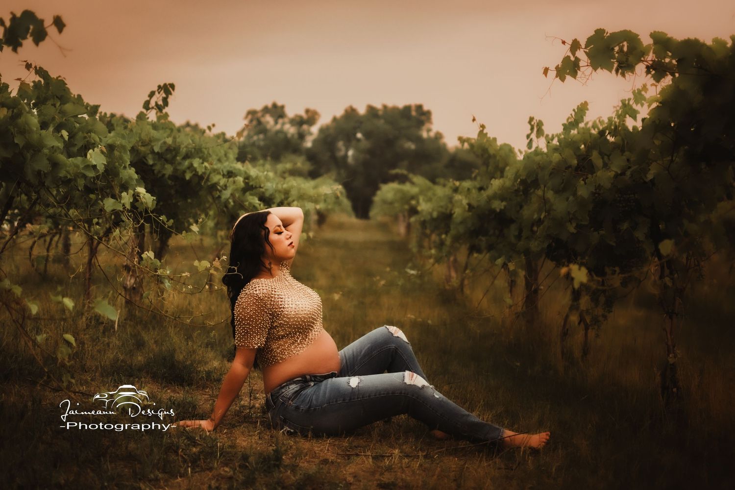 Dreamy maternity pose among vineyard rows during sunset with warm tones.