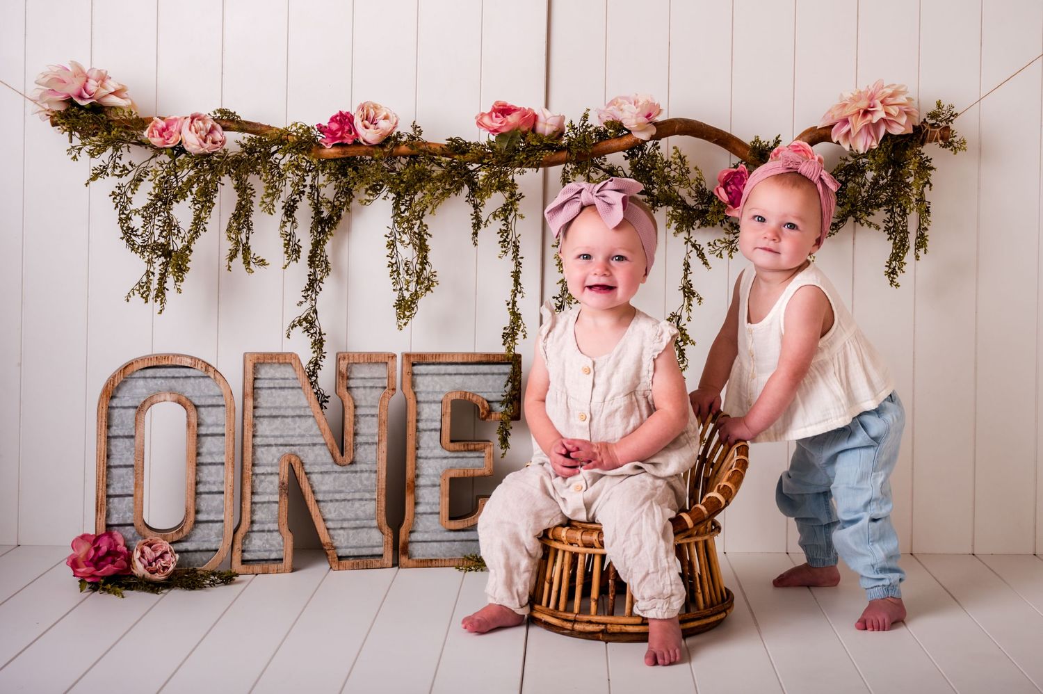 Rustic cake smash setup with pink flowers, greenery garland, and wooden decorations for a first birthday celebration in Kewaskum, WI Studio