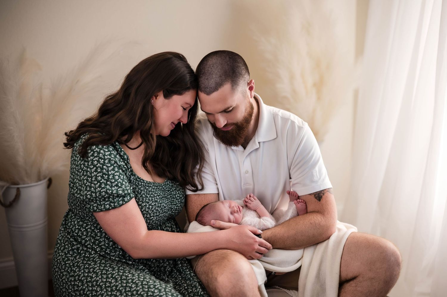 Parents in a bright studio gently embrace their sleeping newborn baby during a cozy lifestyle family photo session.