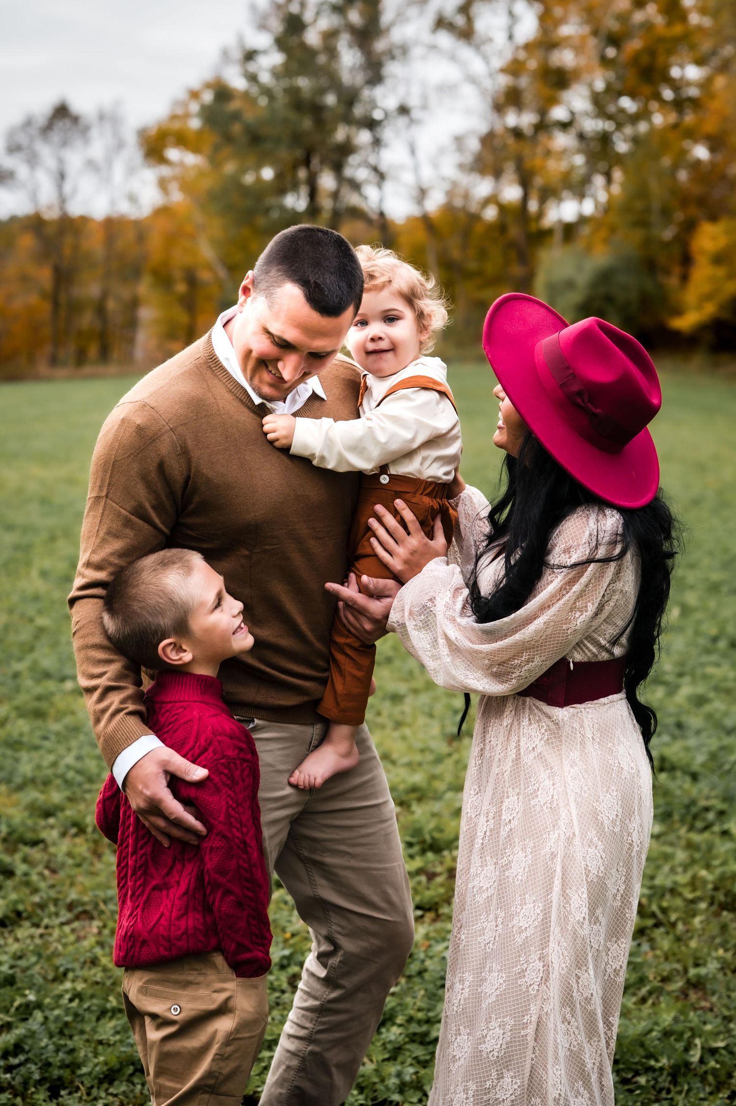 A family shares joyful candid moments together in an autumn field with golden trees in the background, Private Kewaskum Studio, WI