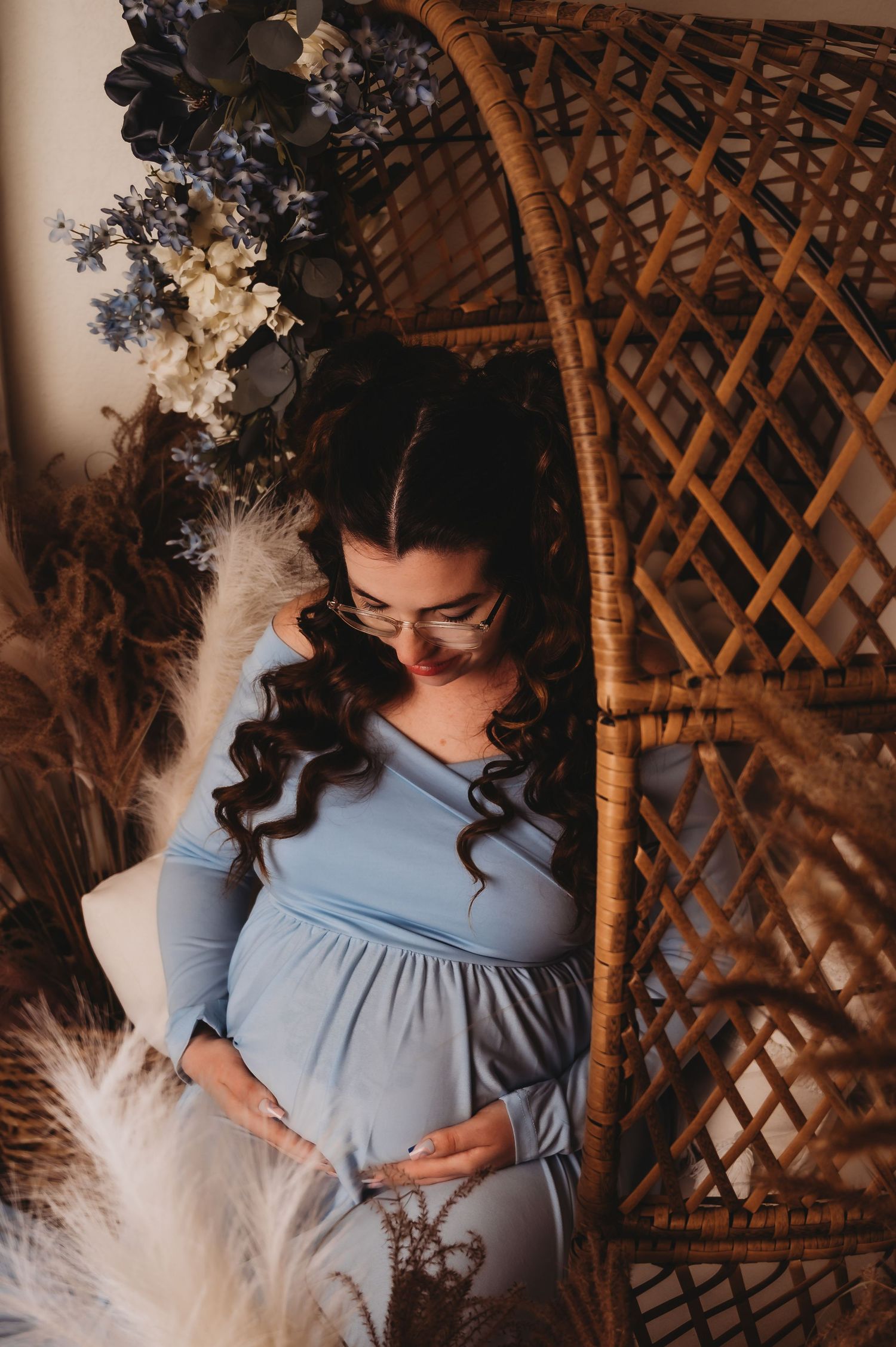 Bohemian maternity portrait with a wicker peacock chair and pampas grass decorations.