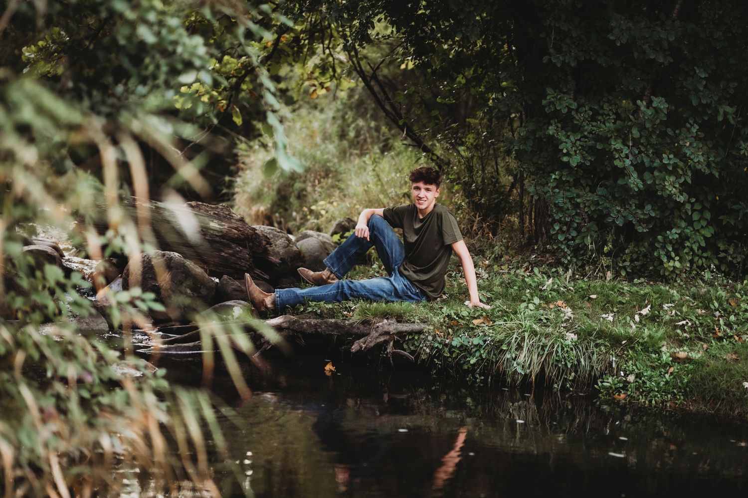 Person relaxing on grassy bank near water's edge in natural setting.
