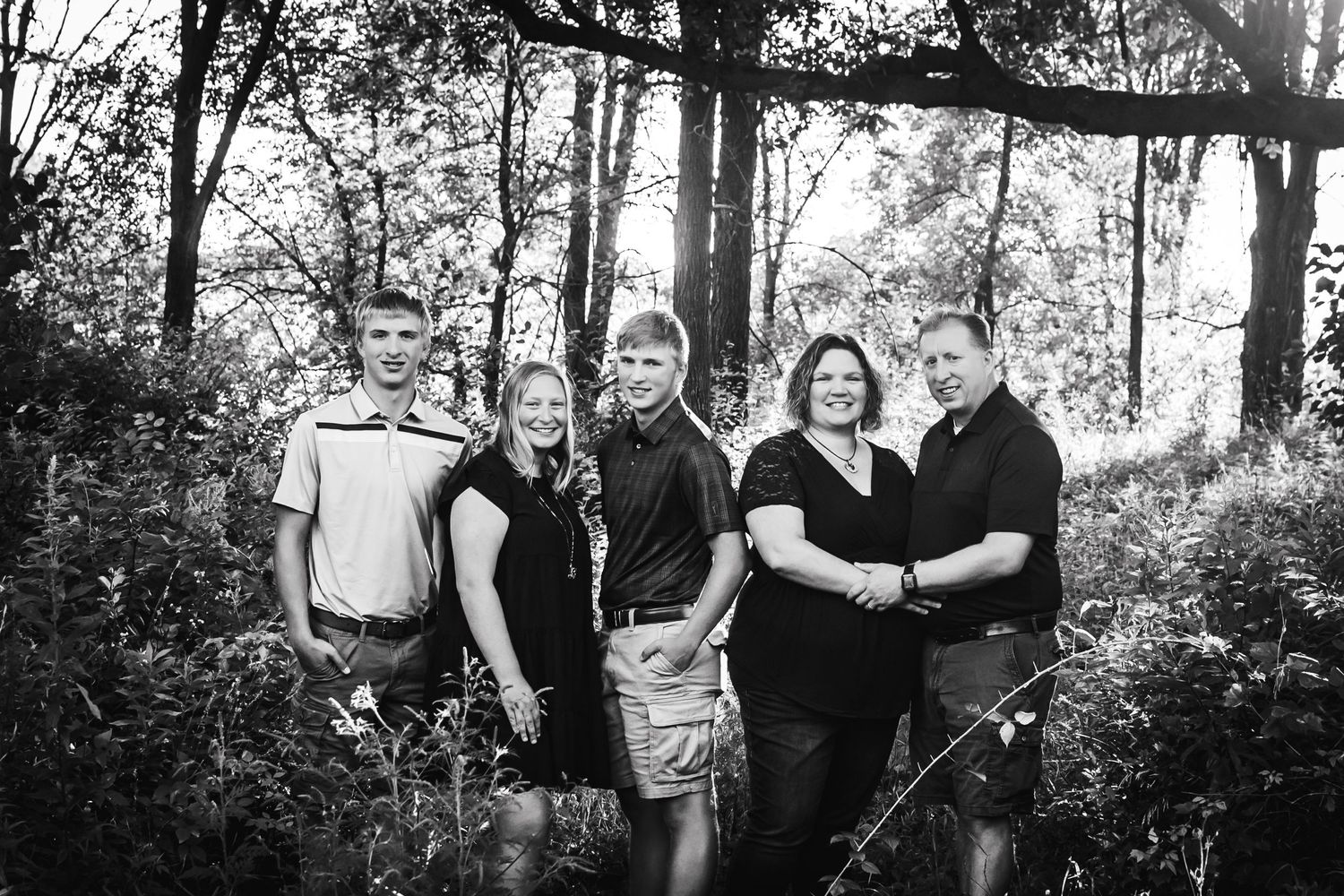 A group of couples pose together for a casual outdoor photo in a wooded setting.