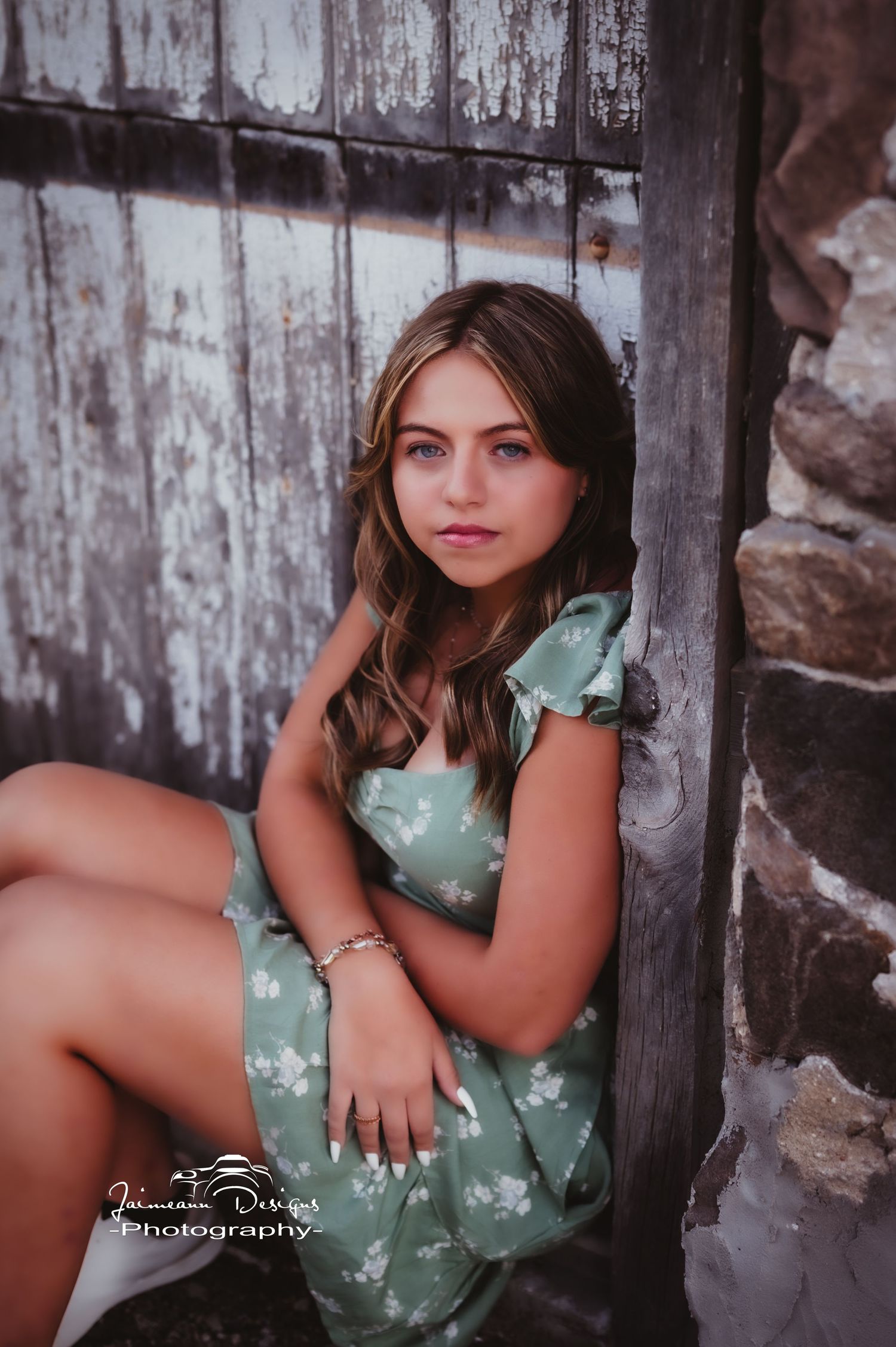 A relaxed portrait featuring someone in a mint floral dress sitting against weathered wood panels.