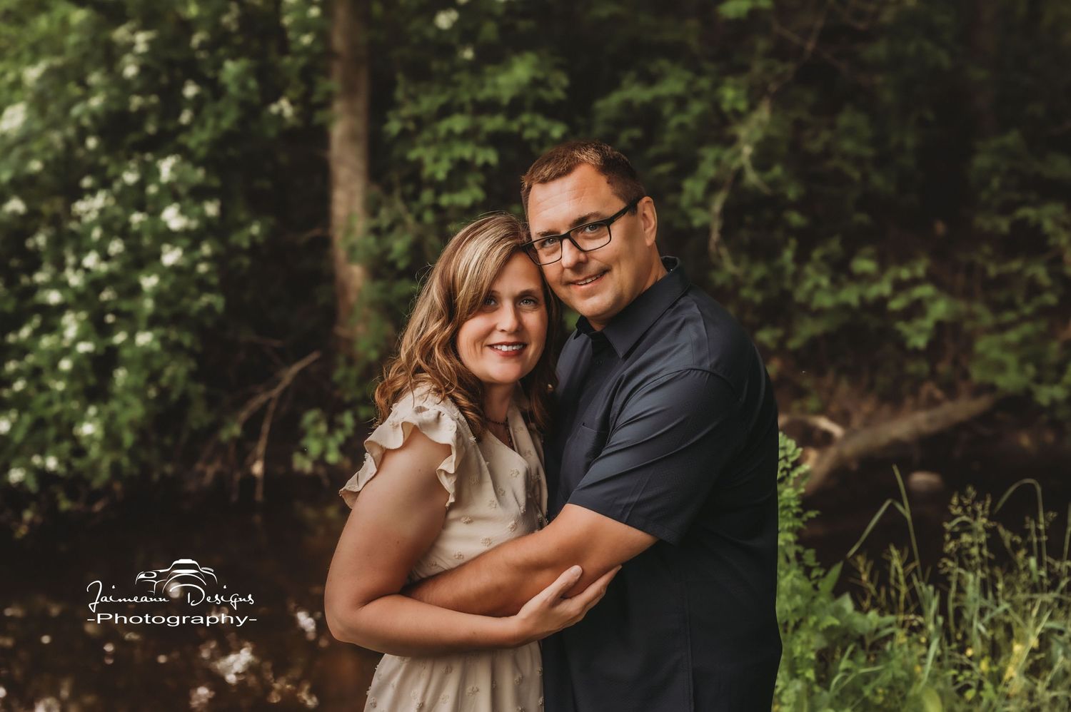 An intimate portrait of a couple embracing in a forest with dappled sunlight.