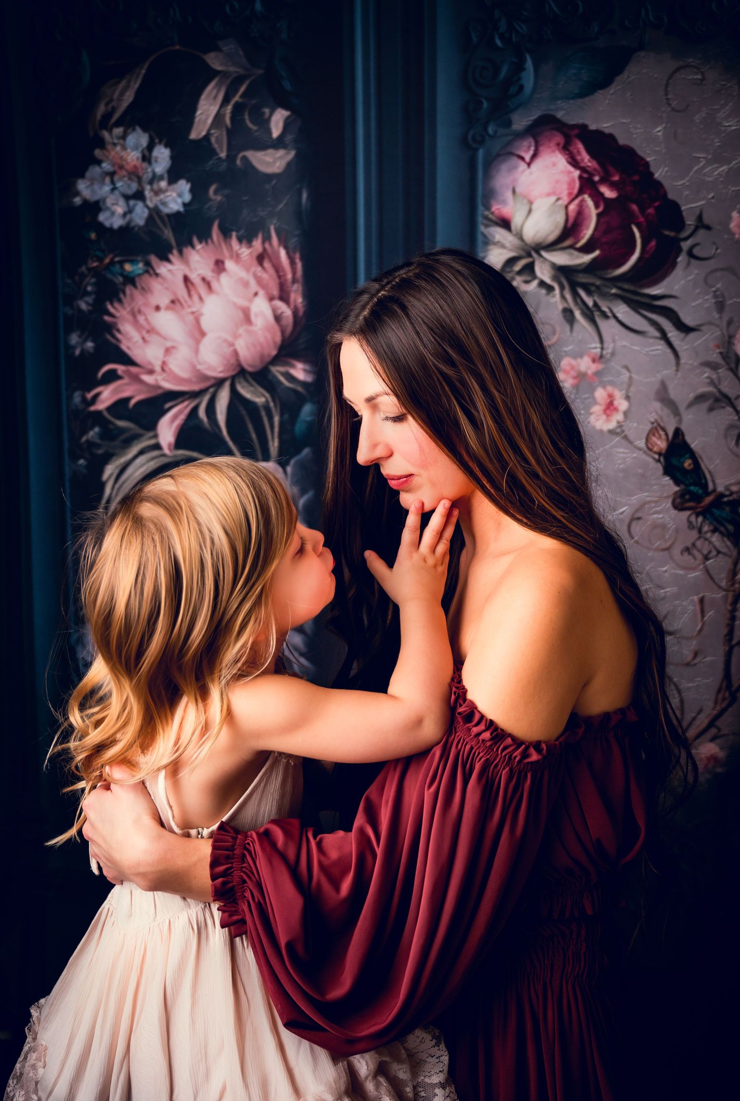 Intimate portrait against moody floral wallpaper with burgundy and cream colored dresses.