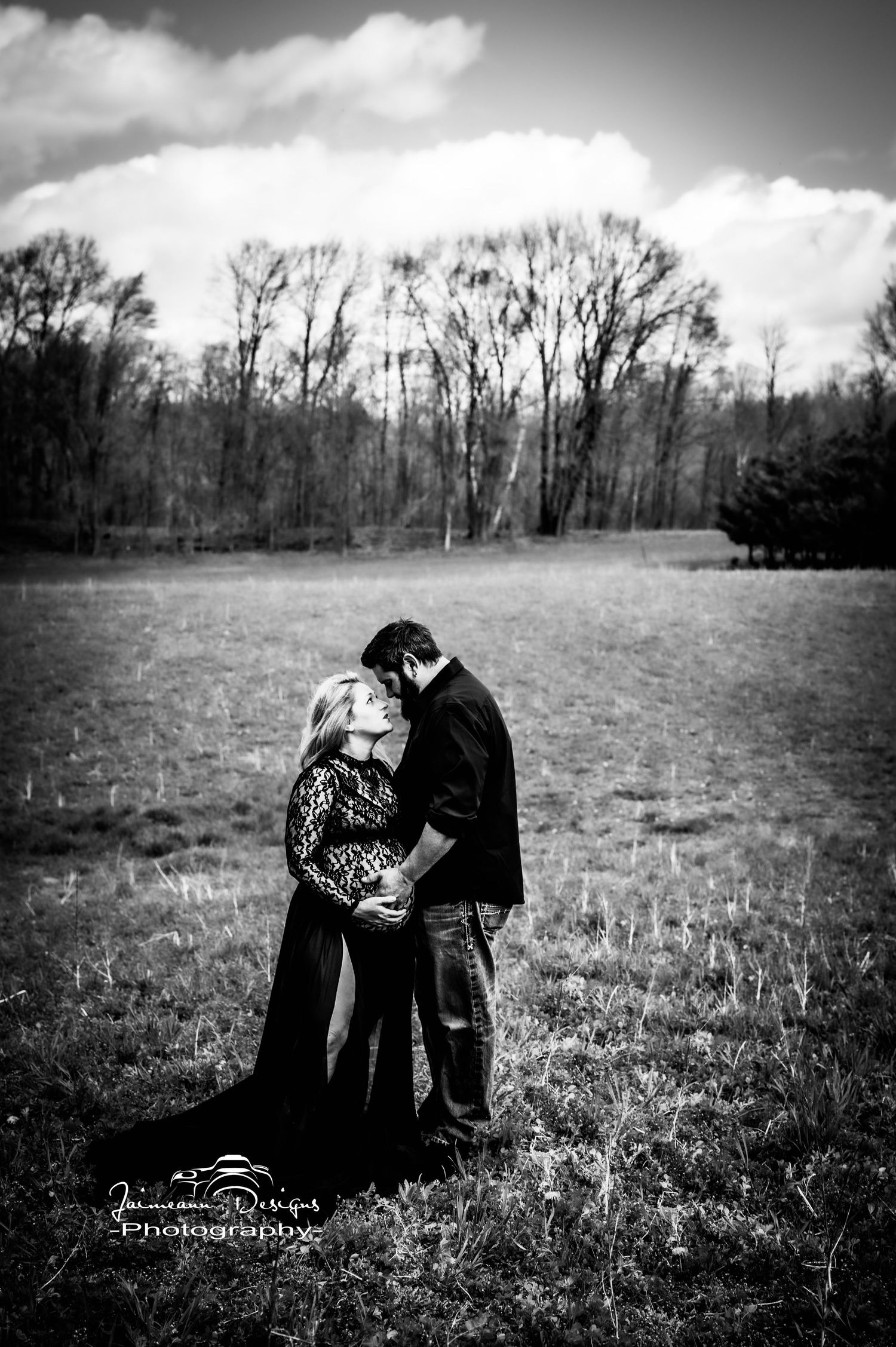 Black and white maternity portrait in open field with dramatic sky.