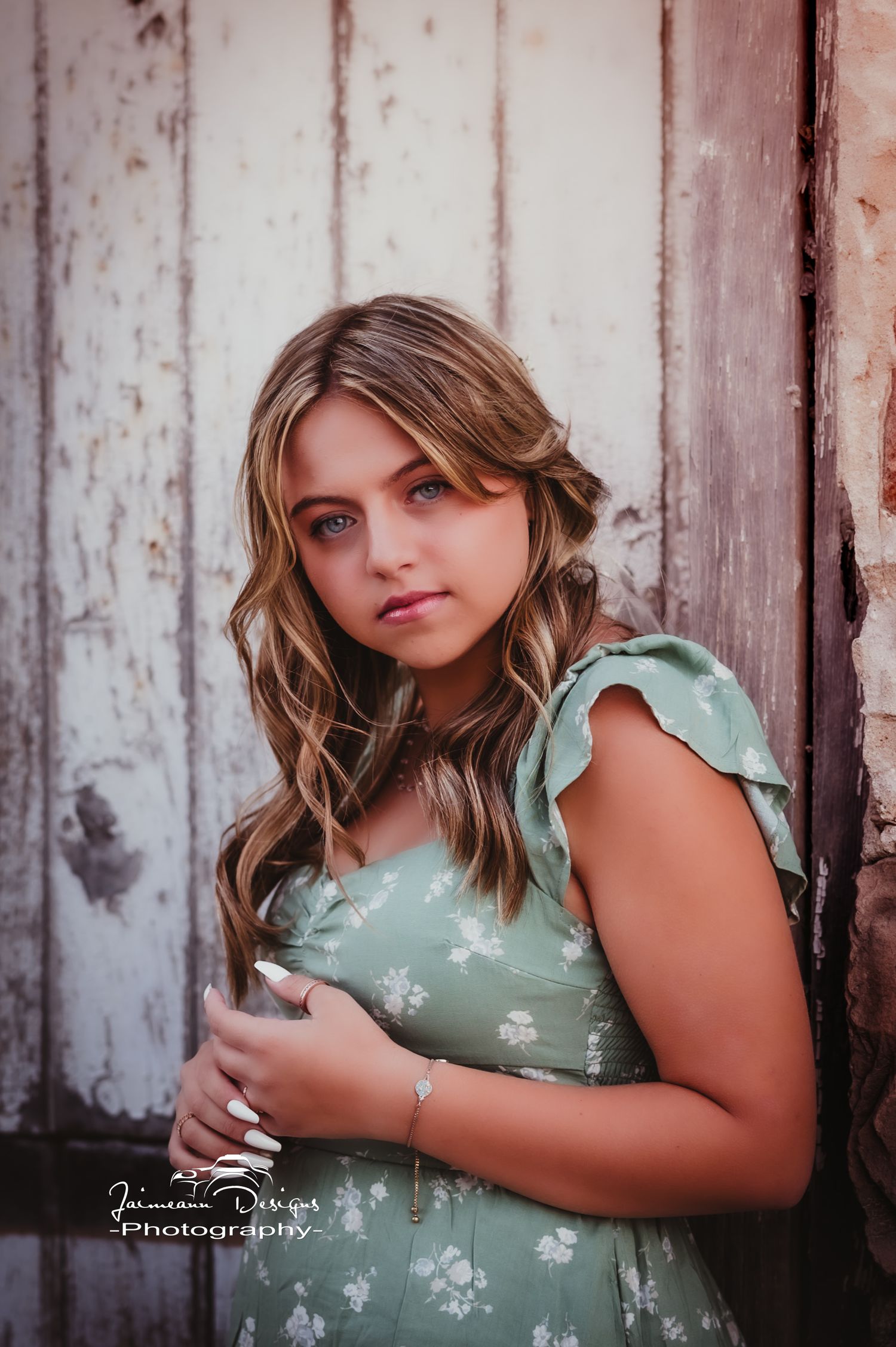 A portrait of someone wearing a mint green floral dress posing against a rustic white wooden wall.