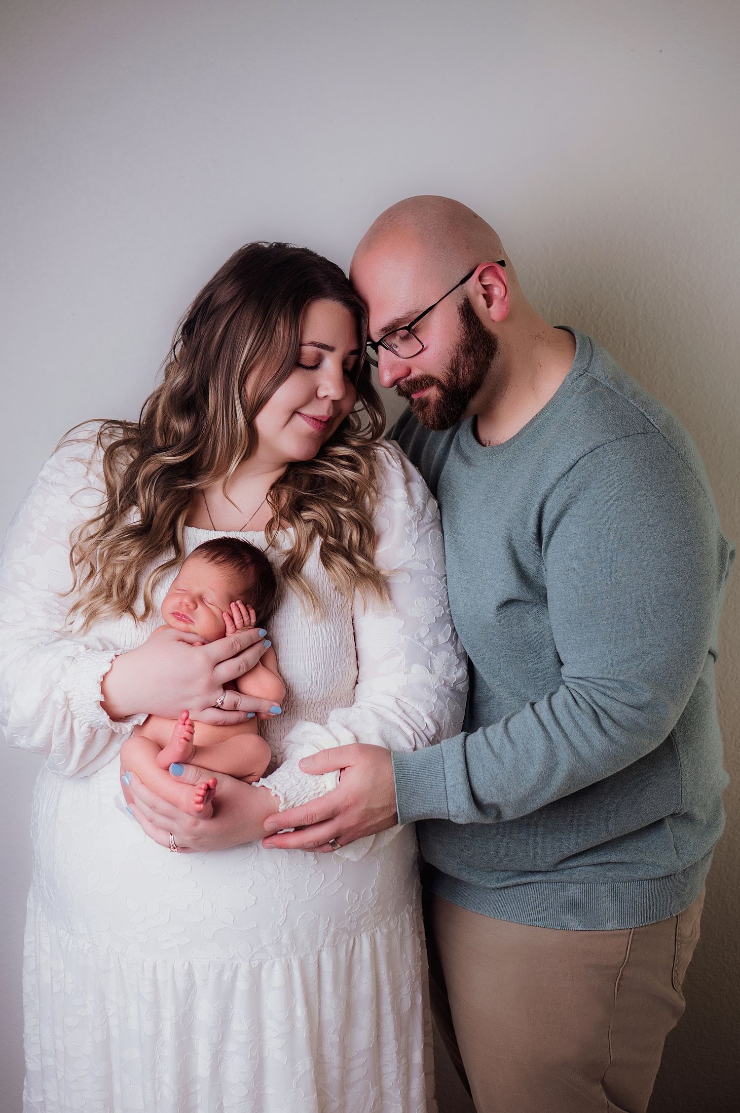 A couple tenderly holds their newborn baby, posing for a professional family portrait against a soft neutral background.