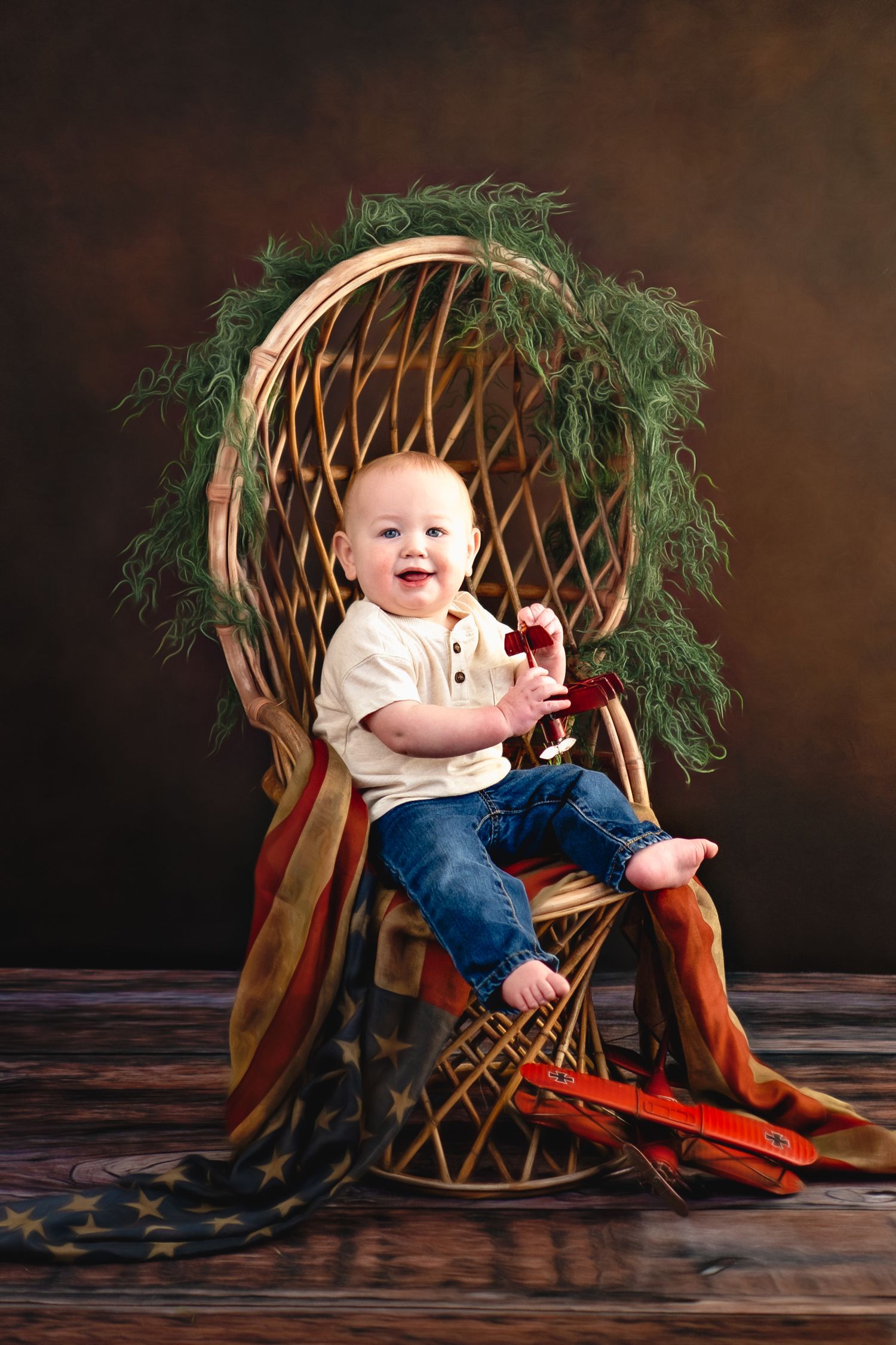 Baby sits in wicker peacock chair with red boots and greenery against dark brown backdrop in photo series near Milwaukee, WI