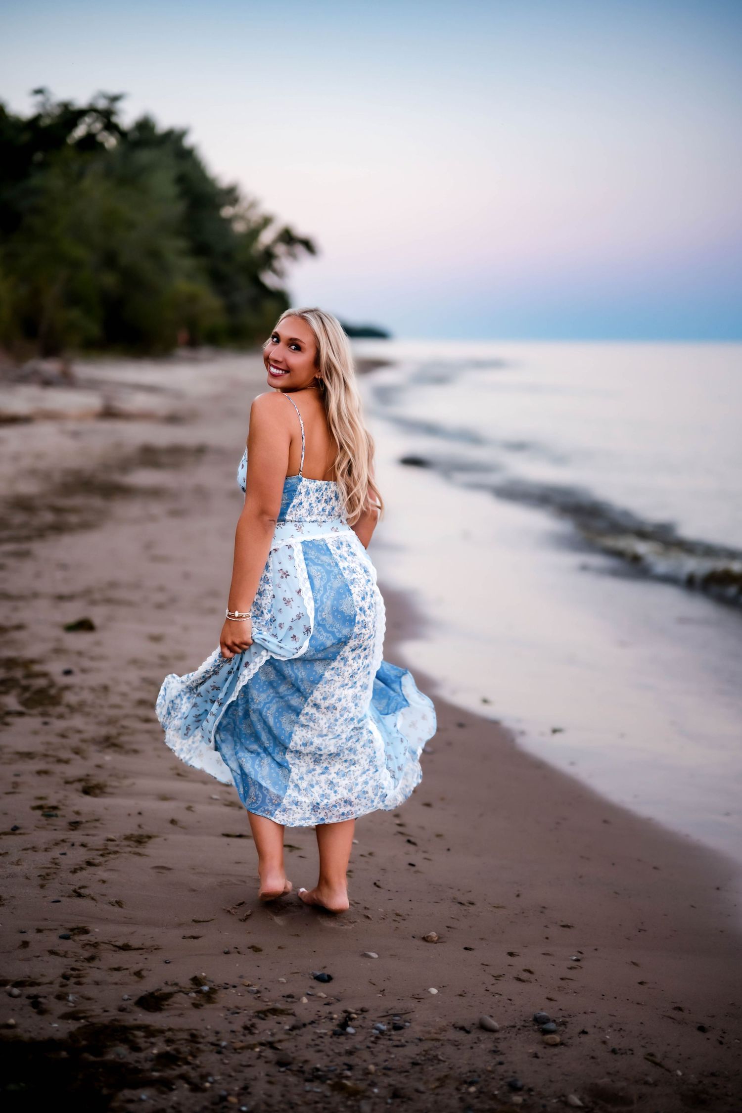 Senior girl twirling her maxi dress and looking back over her shoulder on the beach