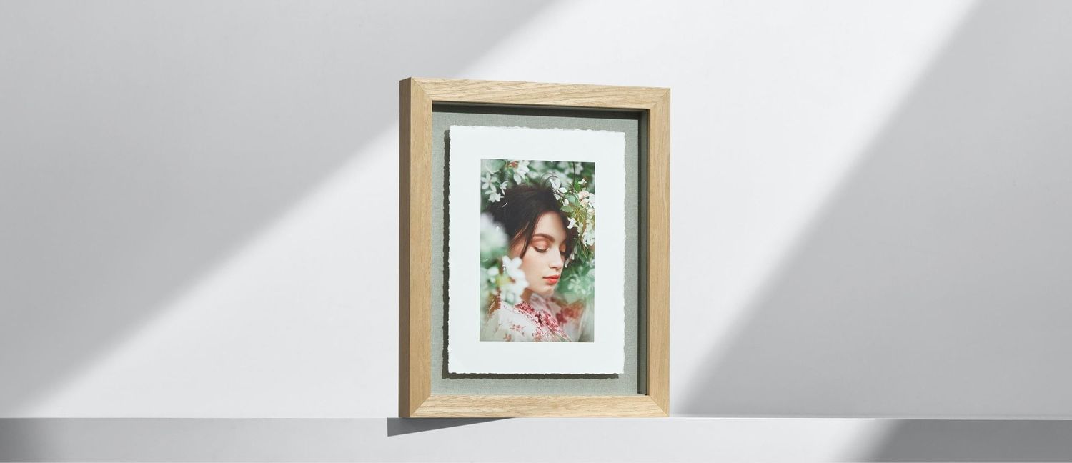 Wooden framed portrait photo of a woman surrounded by flowers, displayed on a light gray surface.