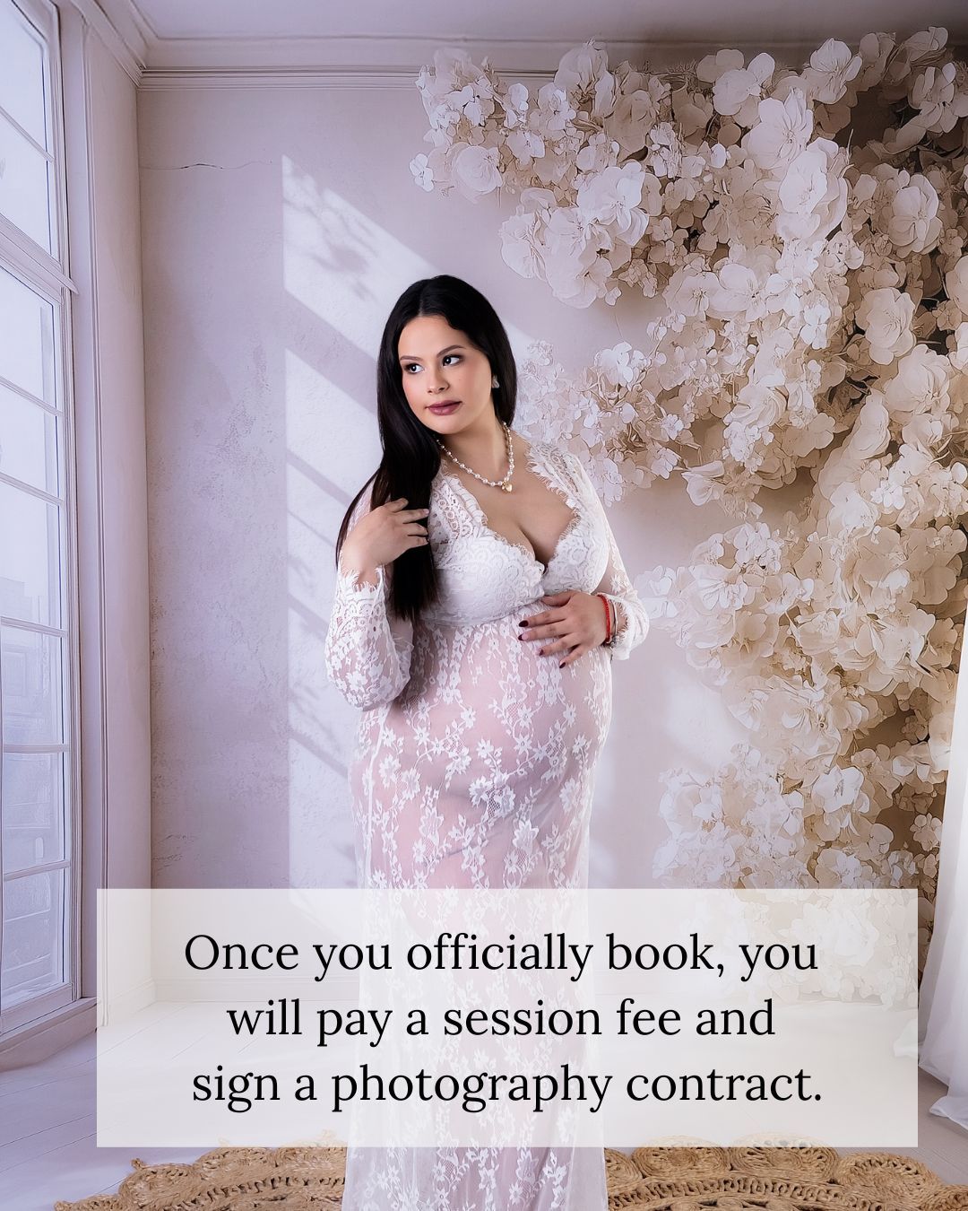 Pregnant woman in white lace maternity gown poses before floral backdrop with text about booking a photography session.