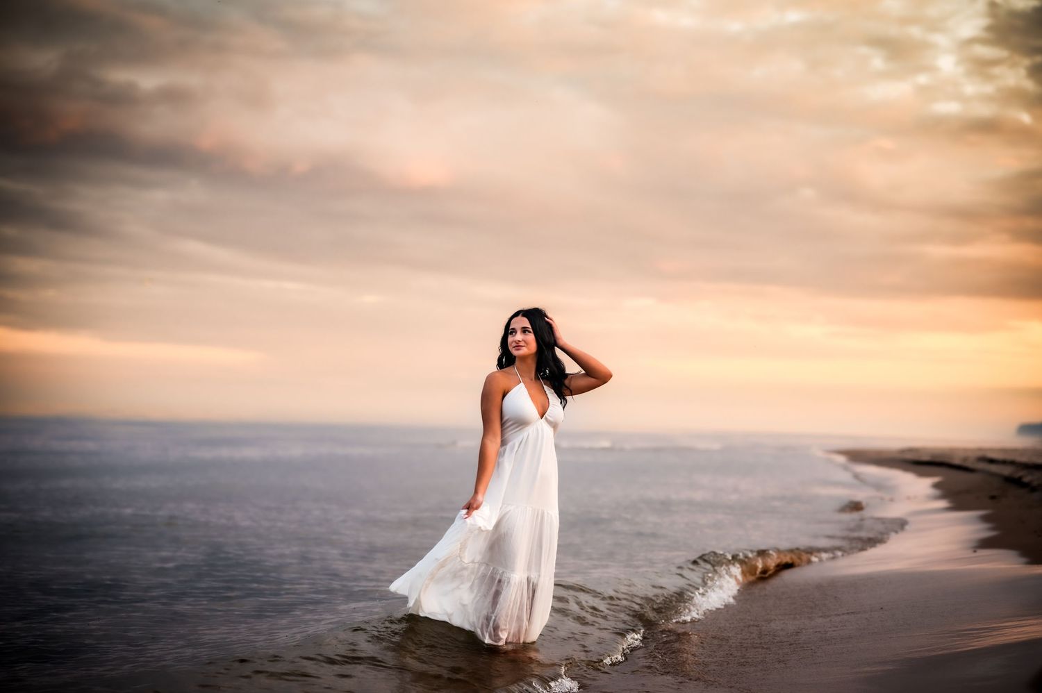 A figure in a flowing white dress walks along a dramatic sunset beach with golden clouds and ocean waves, Kohler Andre State Park, WI