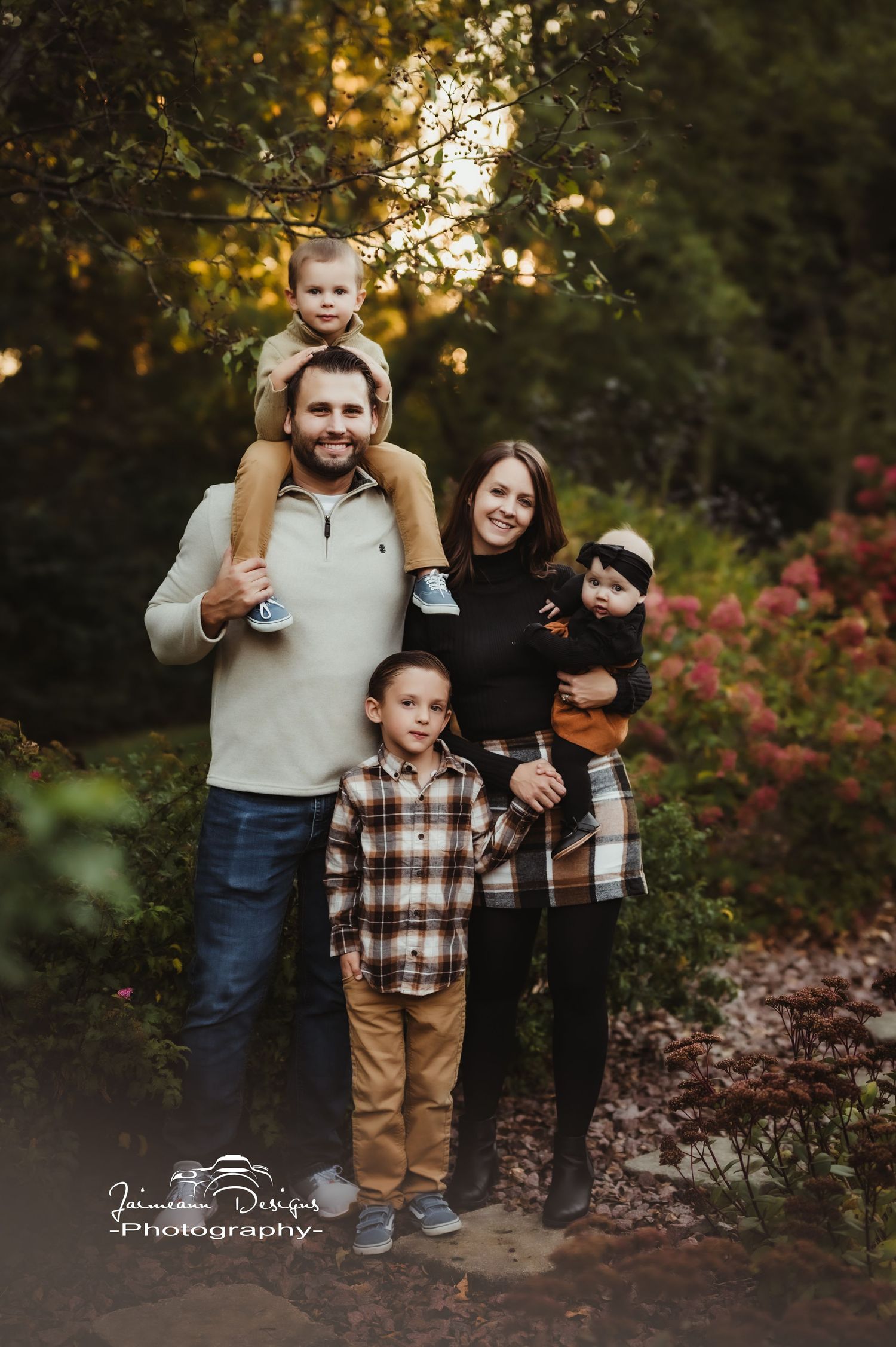 Family of five poses together on woodland path with vibrant fall colors in background.