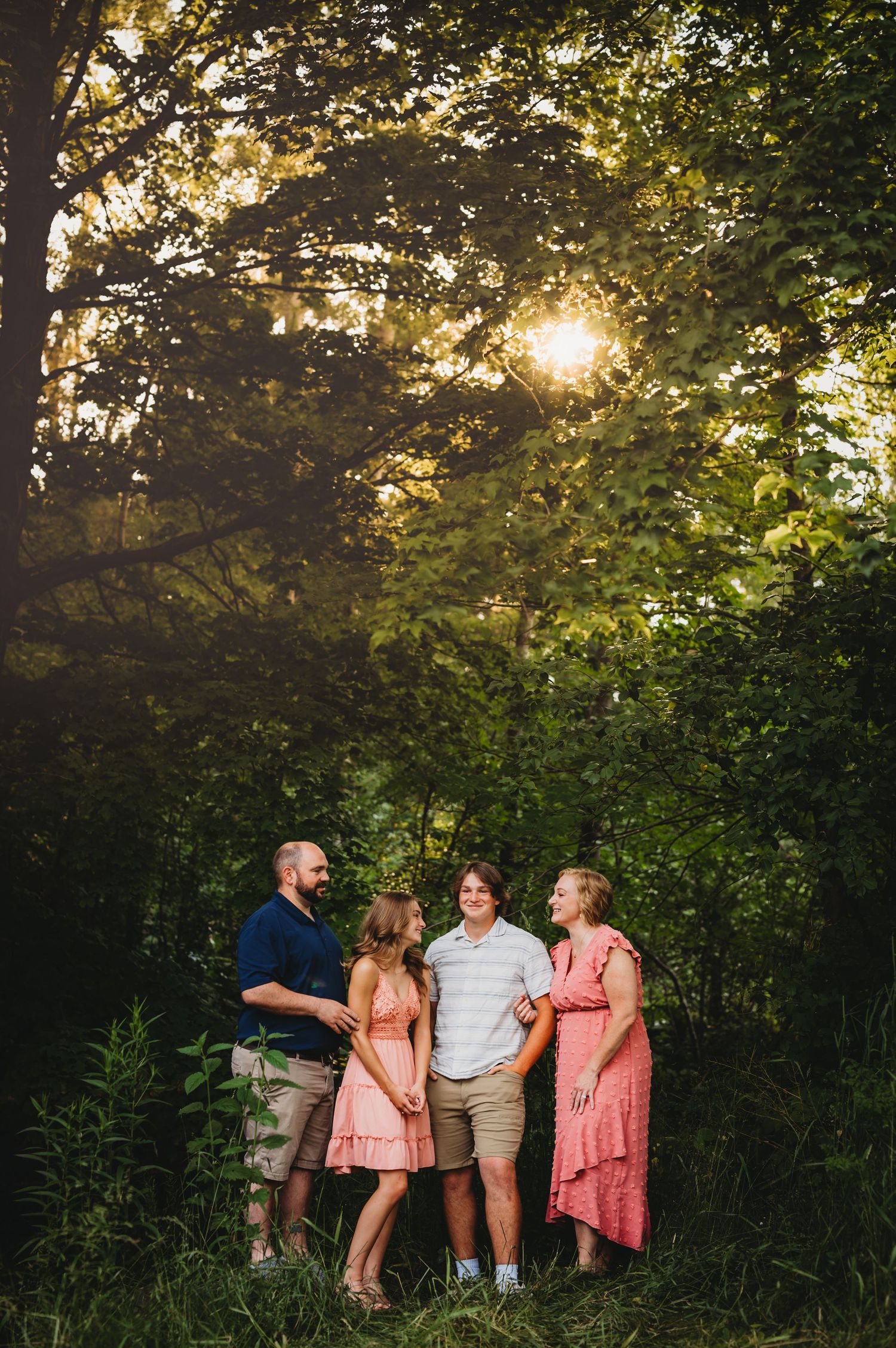 Family group poses together at sunset in wooded clearing with dramatic lighting.