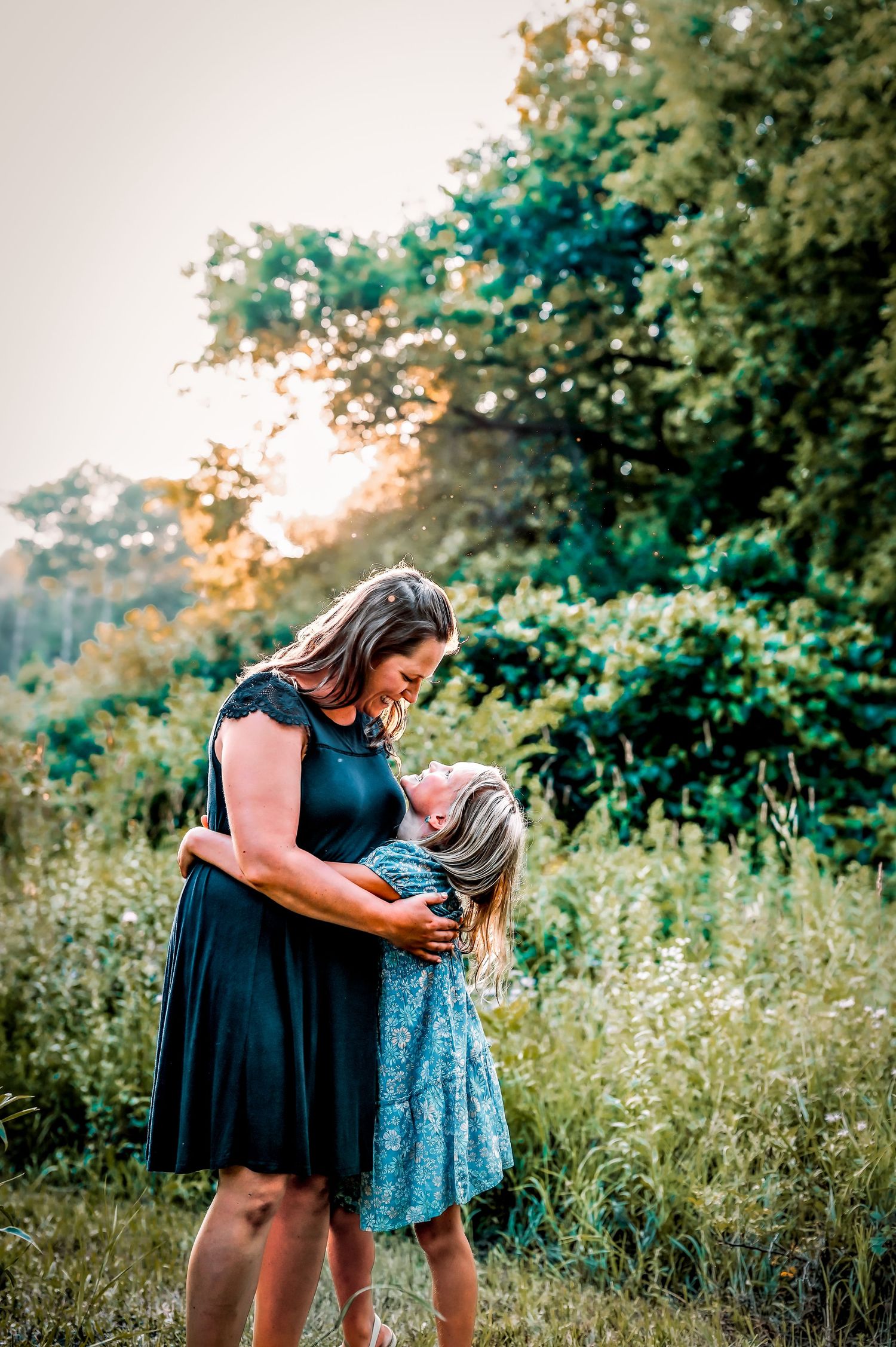 Two people share a tender embrace in a sunlit meadow with wildflowers and trees in the background. West bend, wI