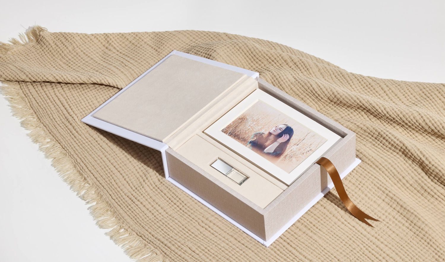 Elegant cream photo box with ribbon, open to reveal a printed photo and USB drive on a woven fabric background Ceadrburg