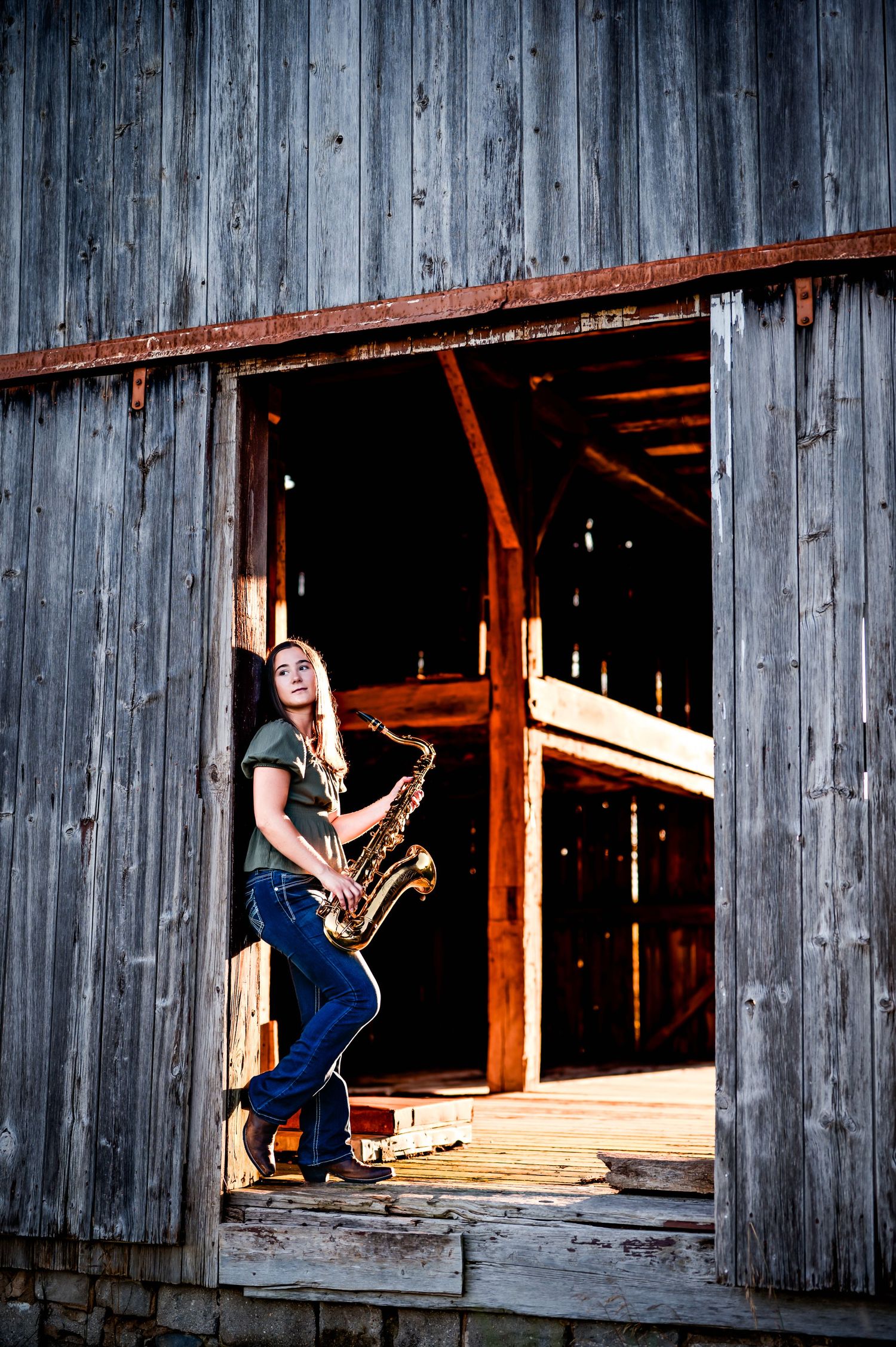 Three musicians perform with guitars and saxophone in rustic barn windows at sunset creating dramatic silhouettes near Kewaskum, WI Studio