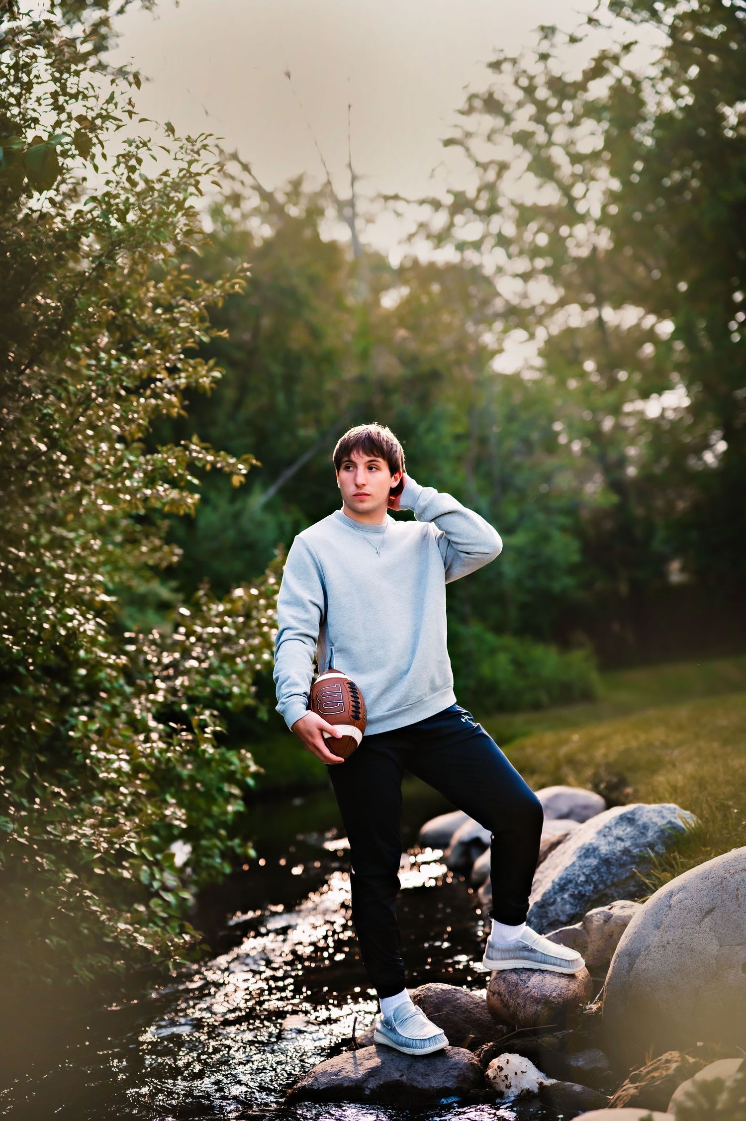A person in a light blue sweater sits on large rocks in a garden setting during golden hour lighting in Regnar Park, WI