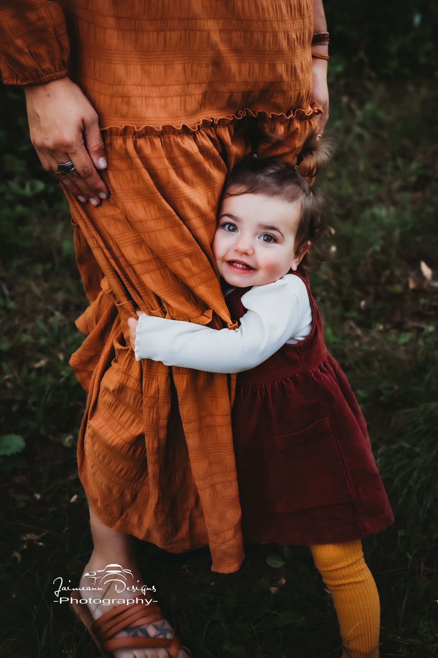 A small child in a burgundy dress and yellow socks hugging someone wearing a rust-colored dress.