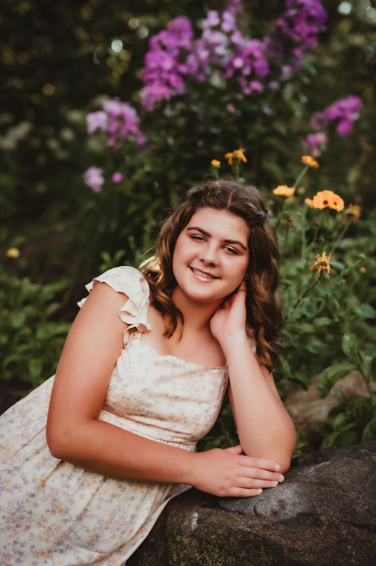Outdoor portrait against colorful garden flowers and natural stone backdrop.