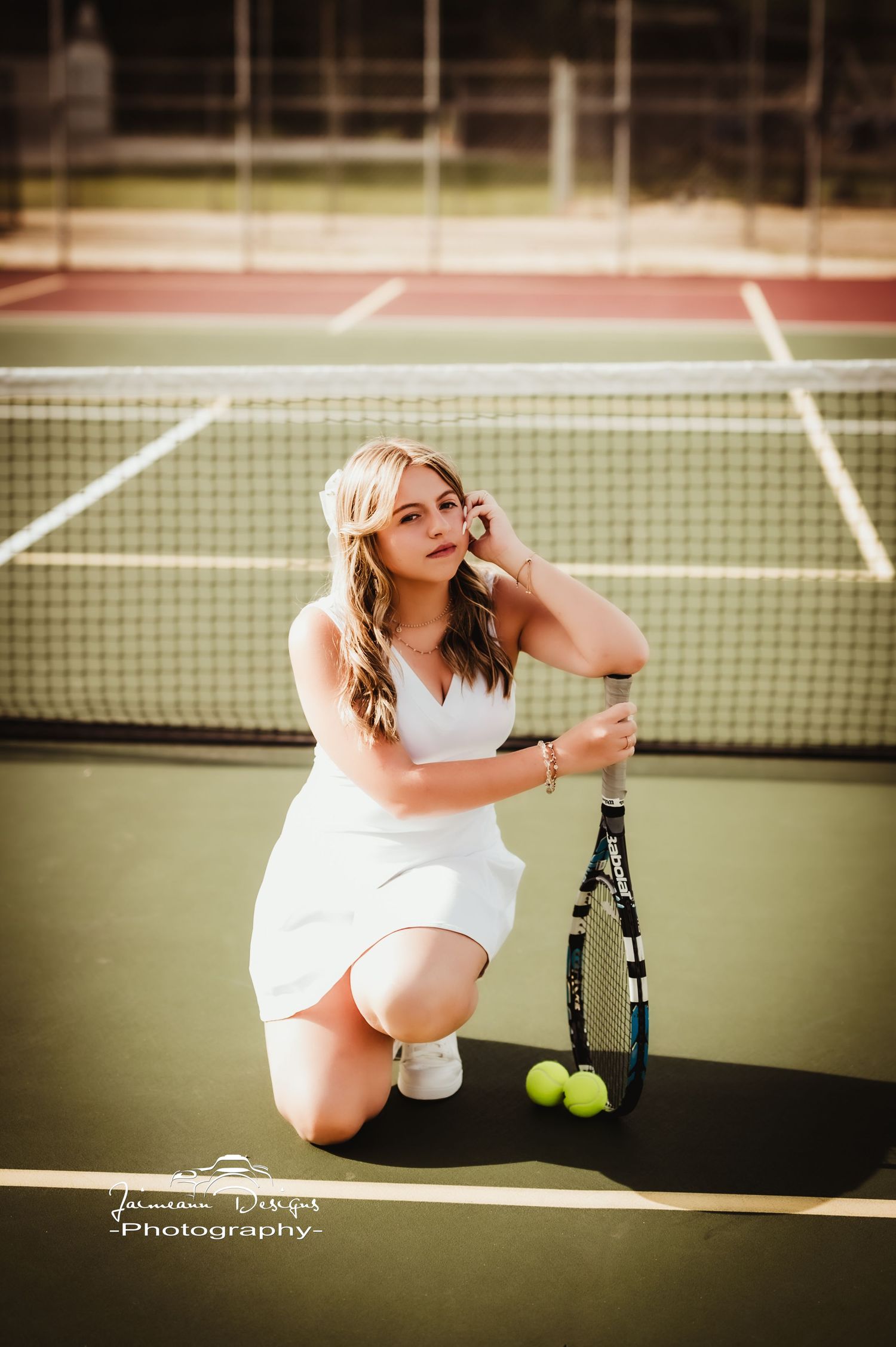 Portrait on a tennis court featuring a white dress and tennis racket with tennis balls on the ground.