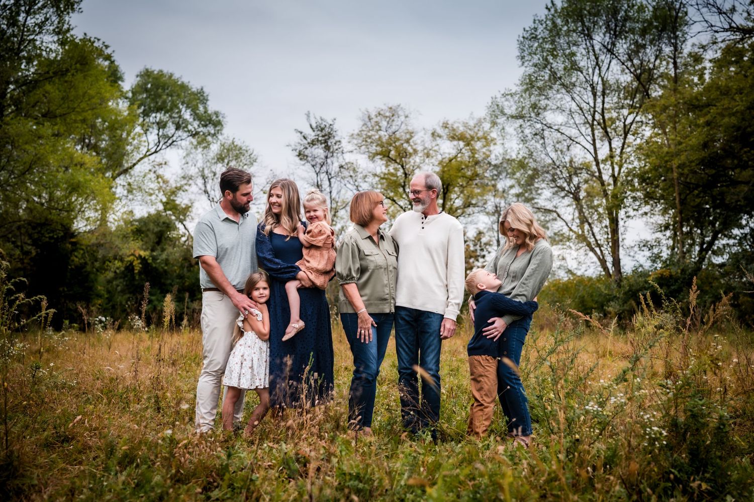 A group of people enjoying a candid moment together outdoors in a grassy field with trees in the background.