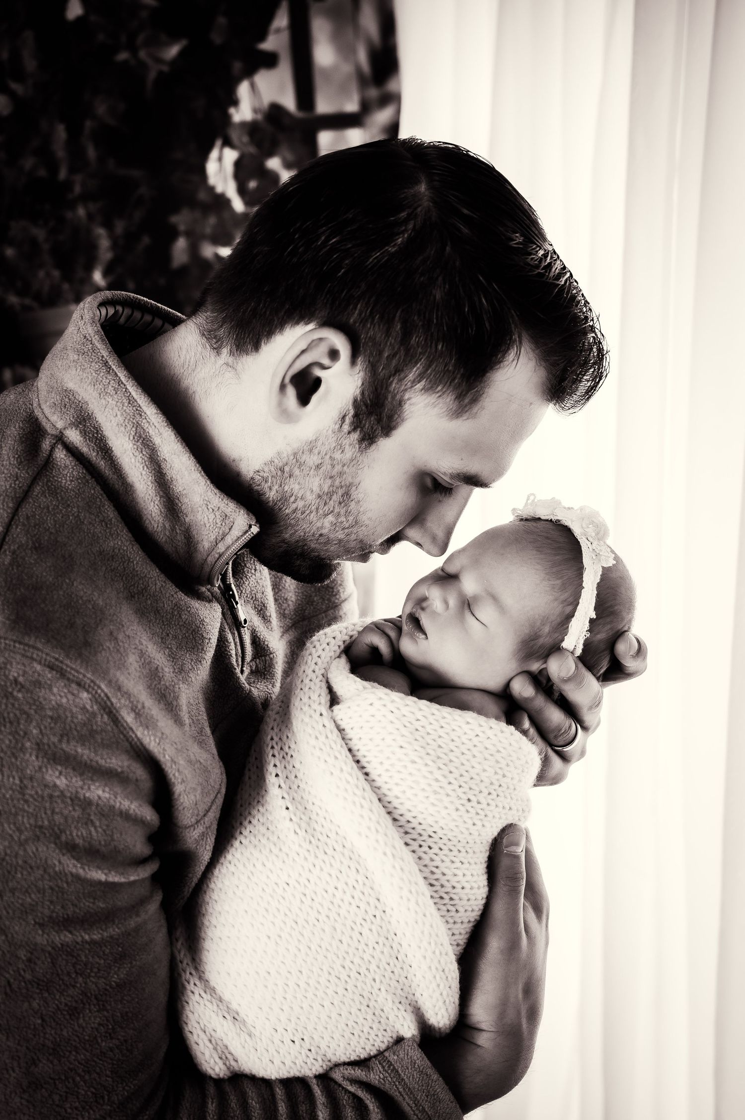 Tender black and white portrait of parent cradling swaddled newborn.