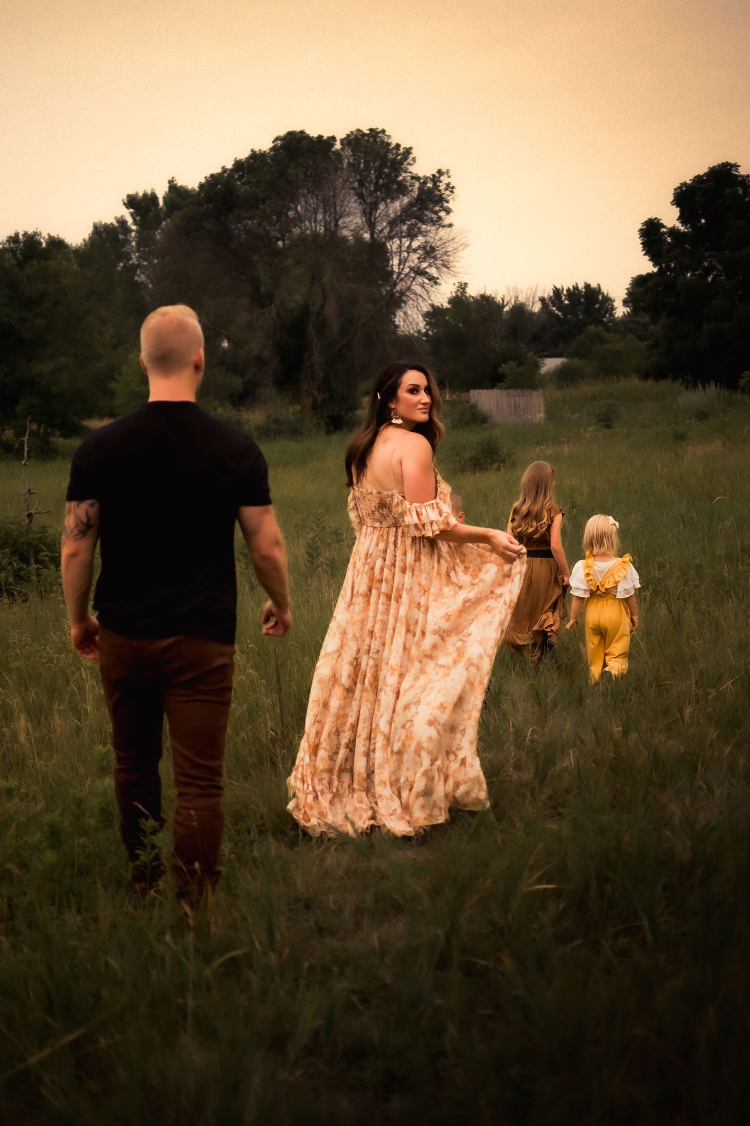 Family walking through meadow at sunset with flowing floral dress.