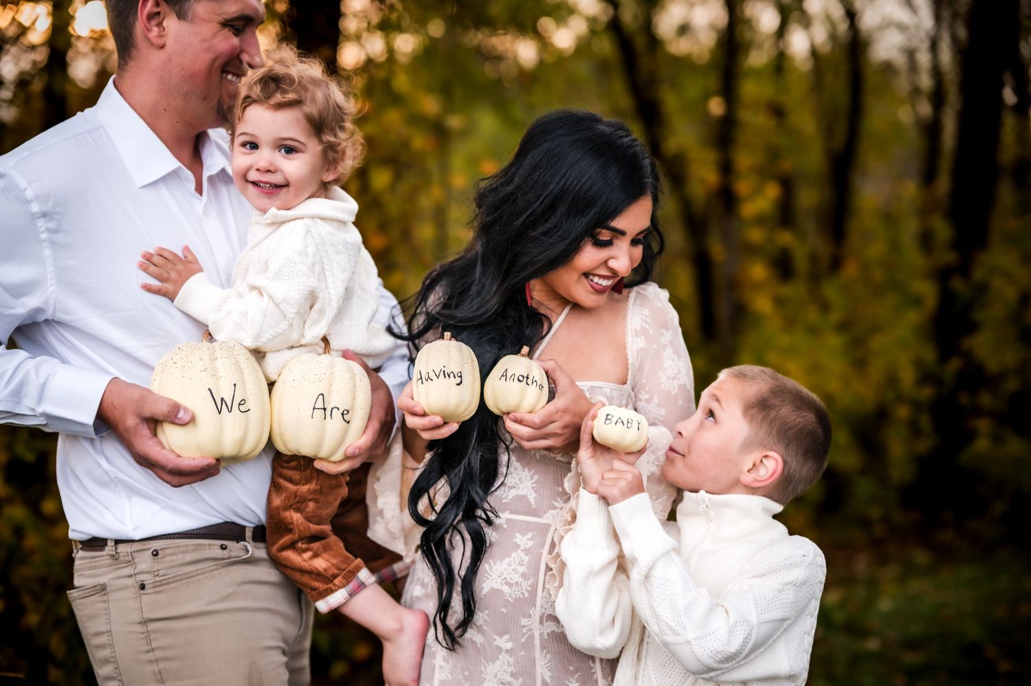 Family pregnancy announcement with pumpkins spelling We Are Having outdoors in autumn setting.