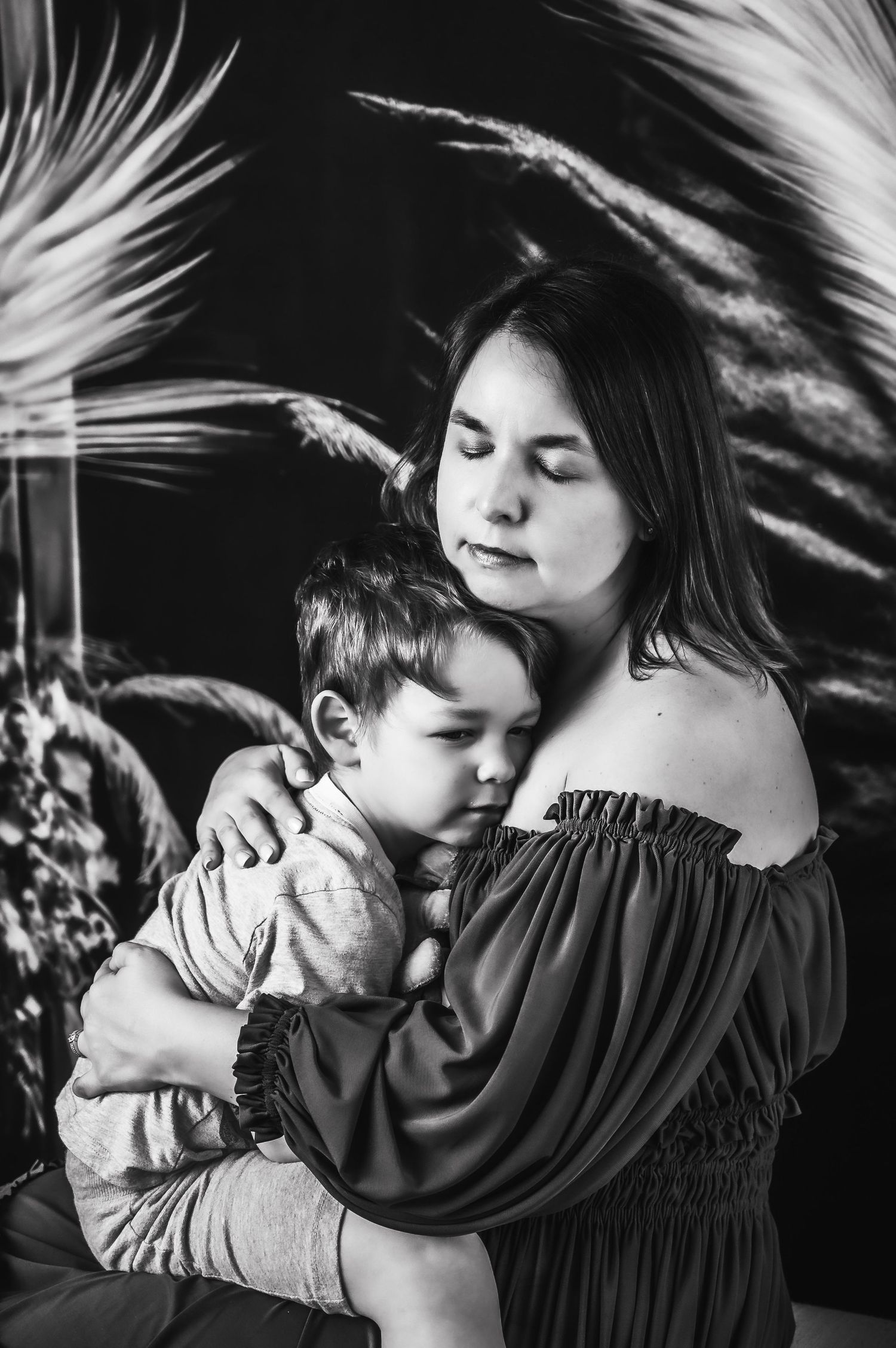 Black and white portrait showing tender embrace against feathered backdrop.