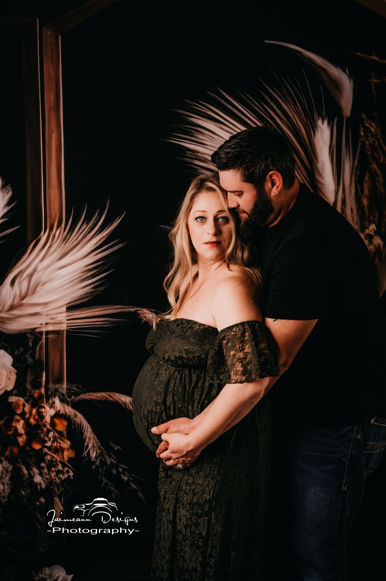 Intimate maternity portrait with dried palm leaves and moody lighting.
