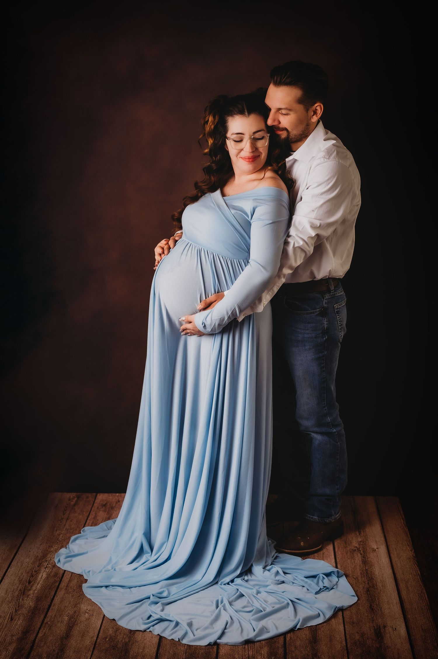 Intimate maternity portrait with flowing blue dress against dark background.