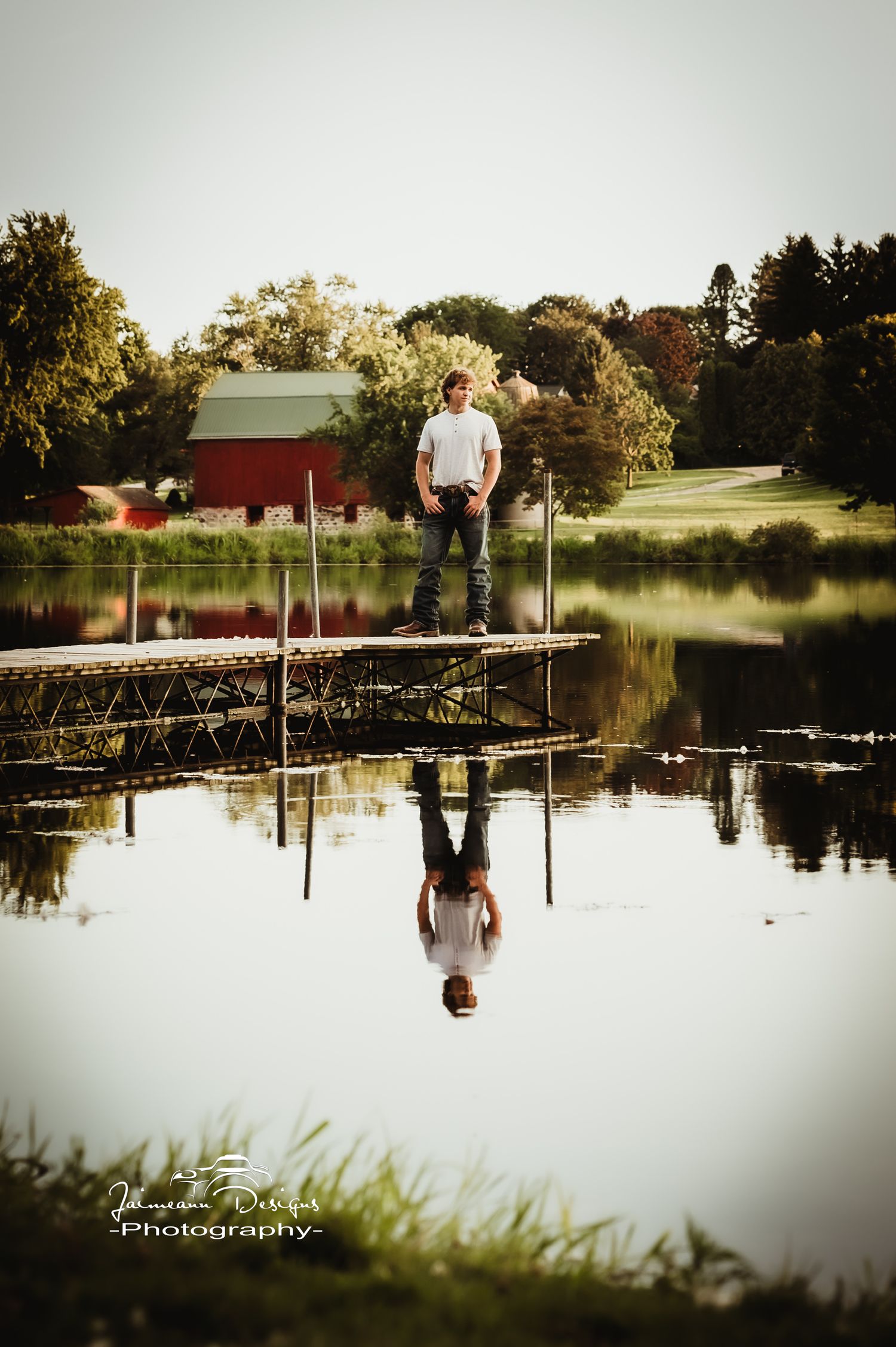 Scenic reflection in pond with red barn and dock in background during sunset.