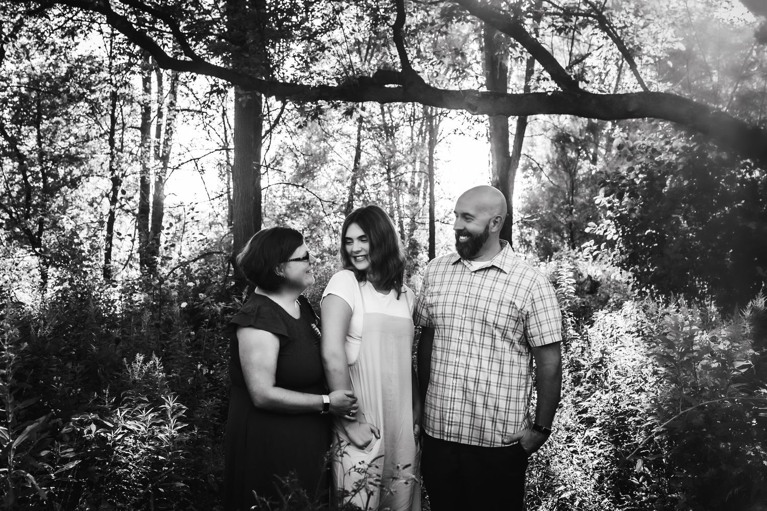 Black and white portrait of three people sharing a close moment under forest trees.