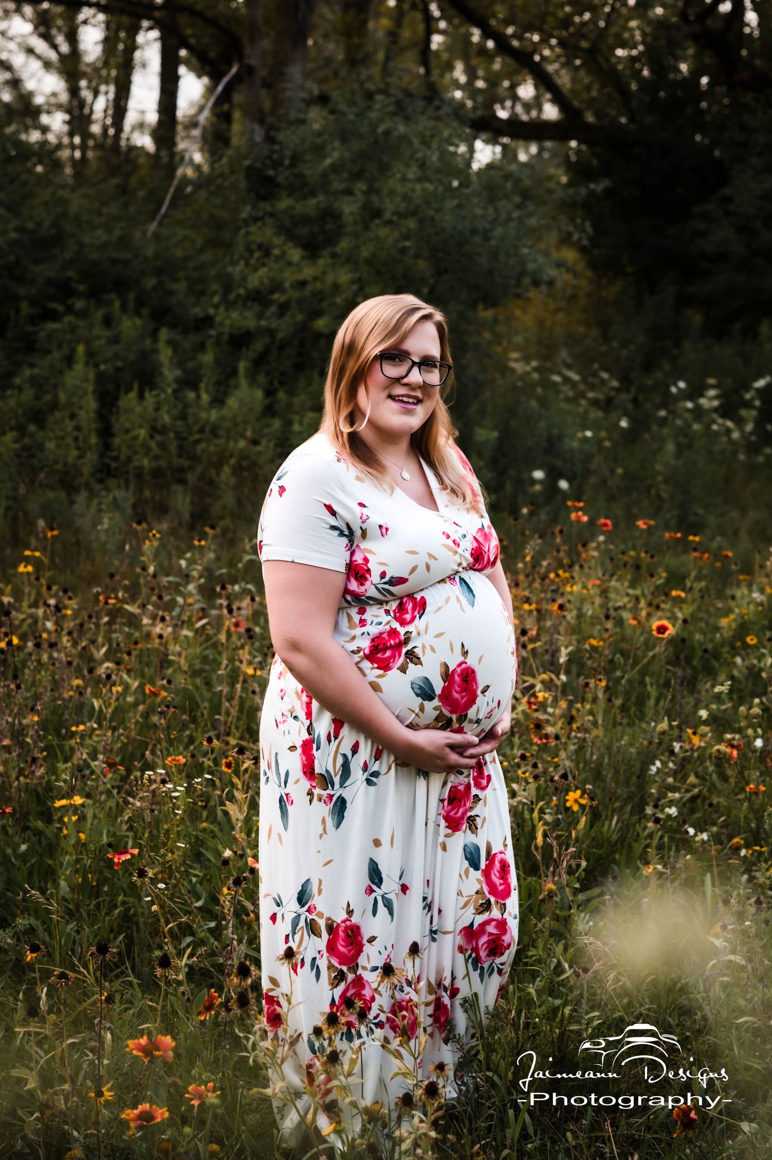 Pregnant woman in floral maxi dress poses in wildflower field for maternity photography session.
